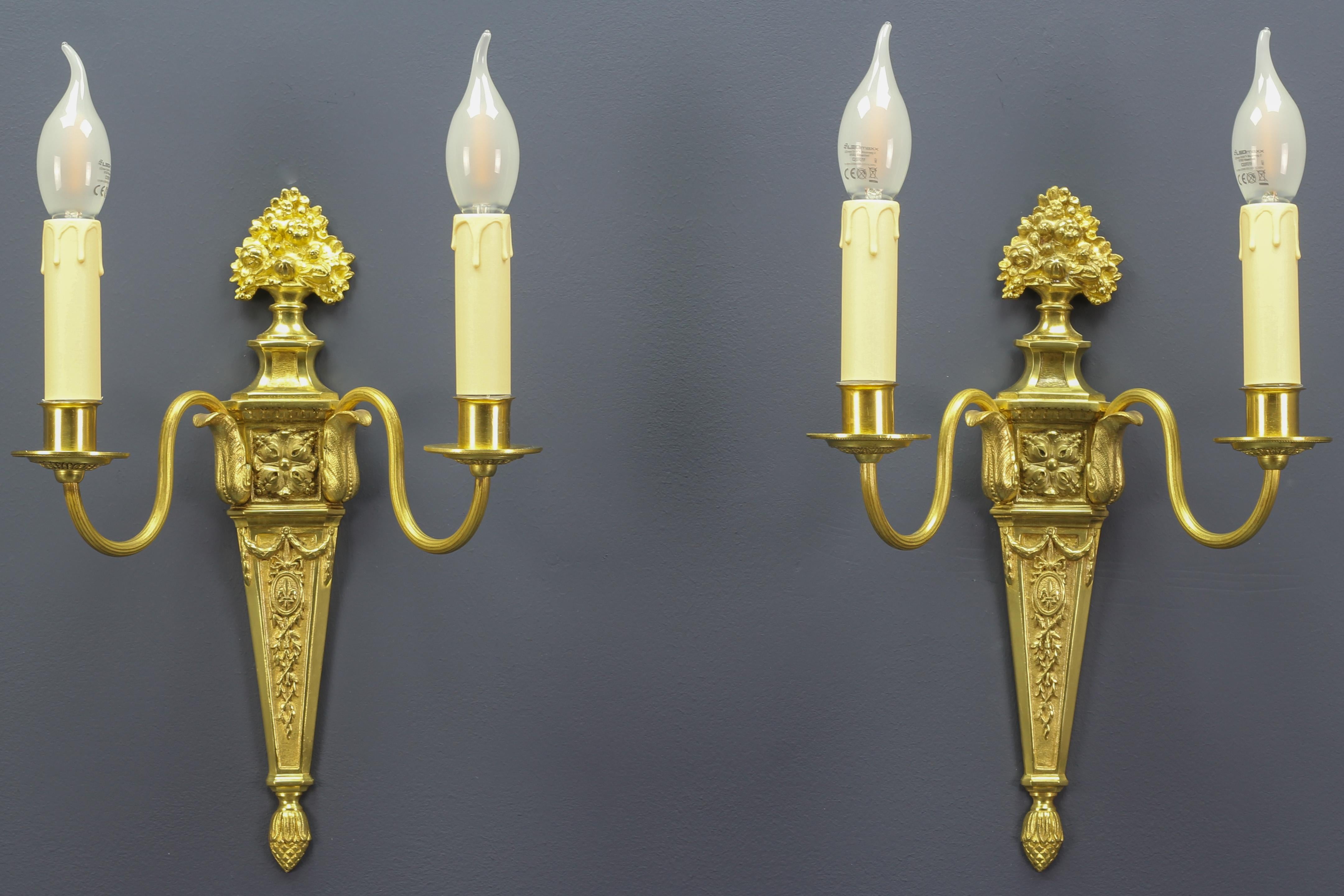 A pair of French early 20th century Louis XVI or neoclassical style gilt bronze and brass sconces. Wall lights have been electrified later. Richly decorated with bronze details, like flowers, acanthus leaves, royal French lily, fleur-de-lis, and