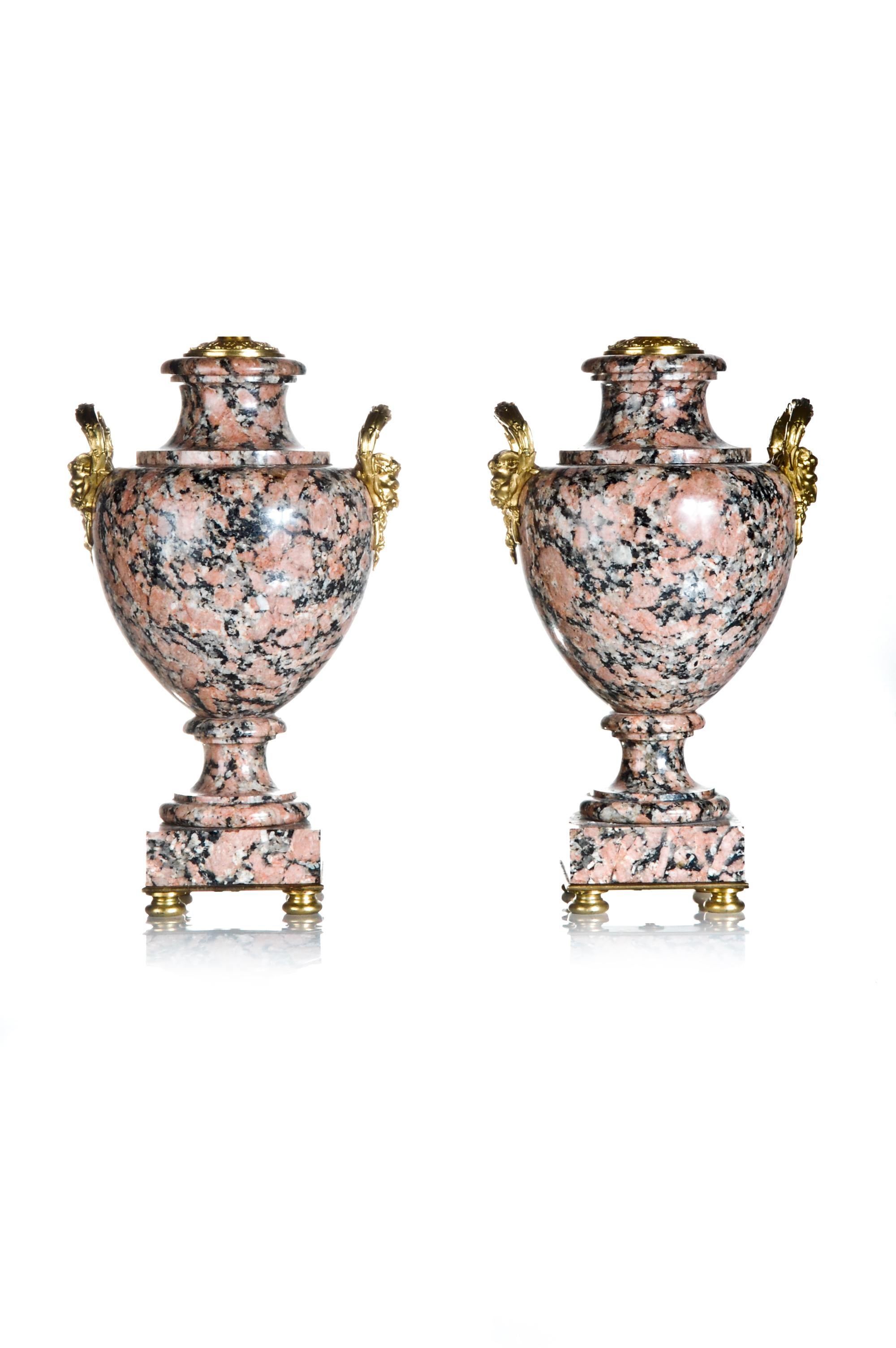 A pair of unique French Louis XVI Style urn form gilt bronze mounted pink and black granite lamps on square bases embellished with gilt bronze figural masks on the sides.