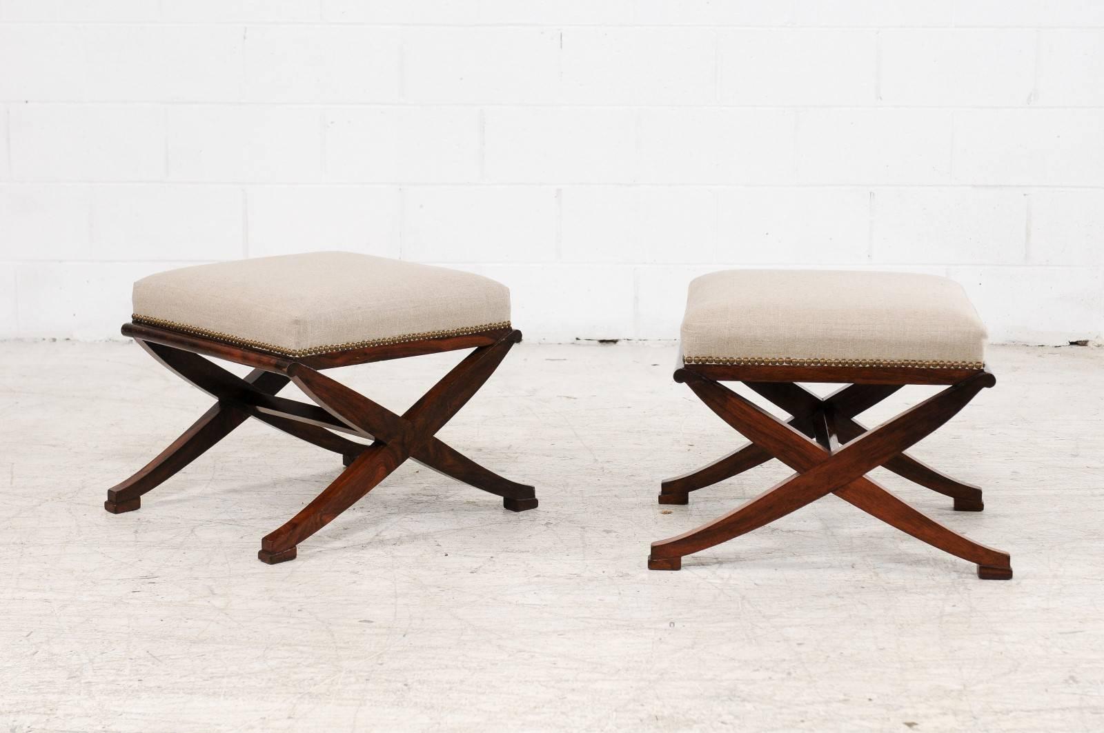 A pair of French mahogany or rosewood X-form stools from the second half of the 19th century with re-upholstered seats. Each of this pair of French stools features an almost square seat covered with a new linen upholstery, accented with a brass
