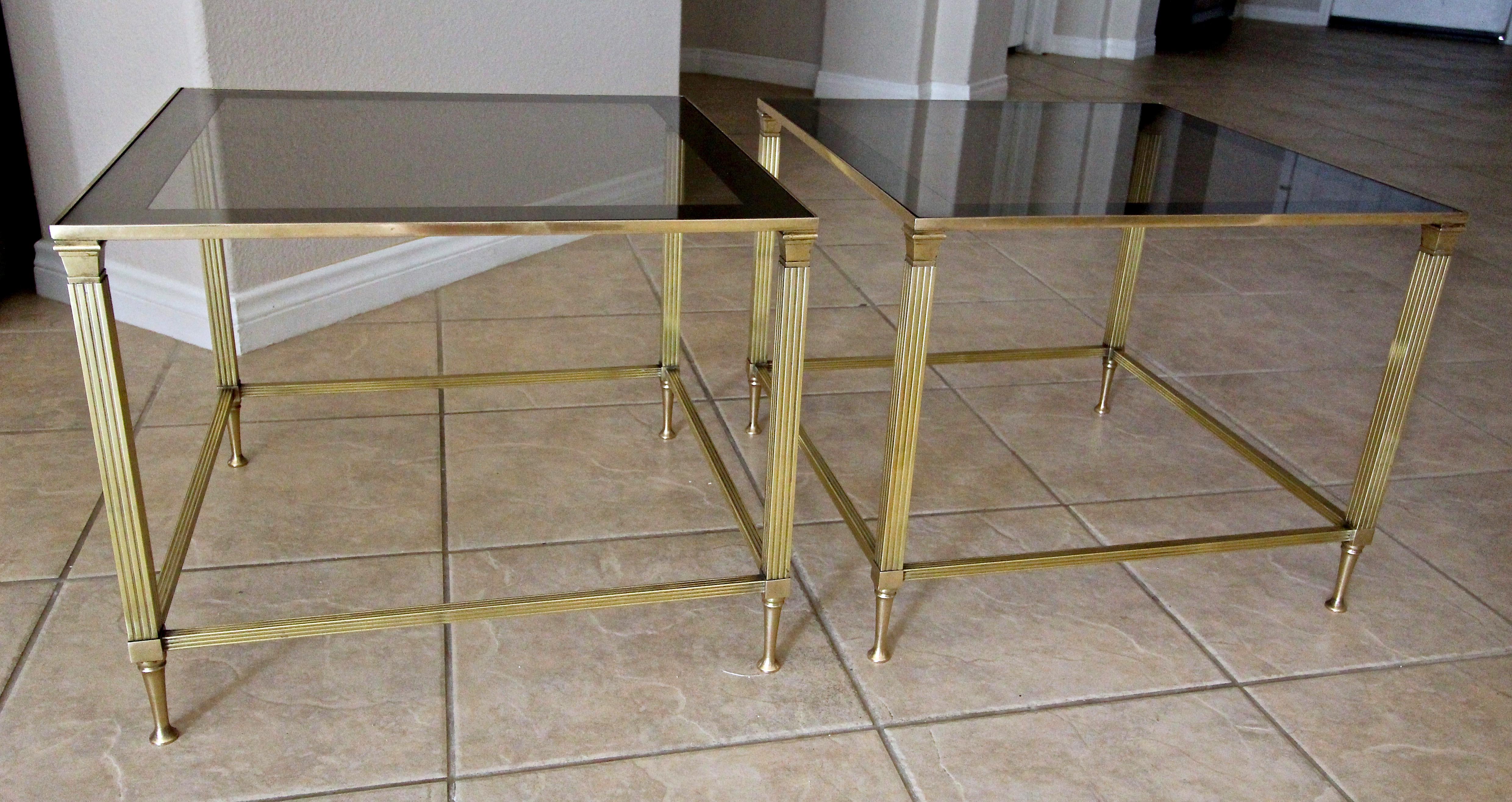 A pair of French brass side tables with smoked mirrored edge glass inset tops, by well known maker Maison Jansen.