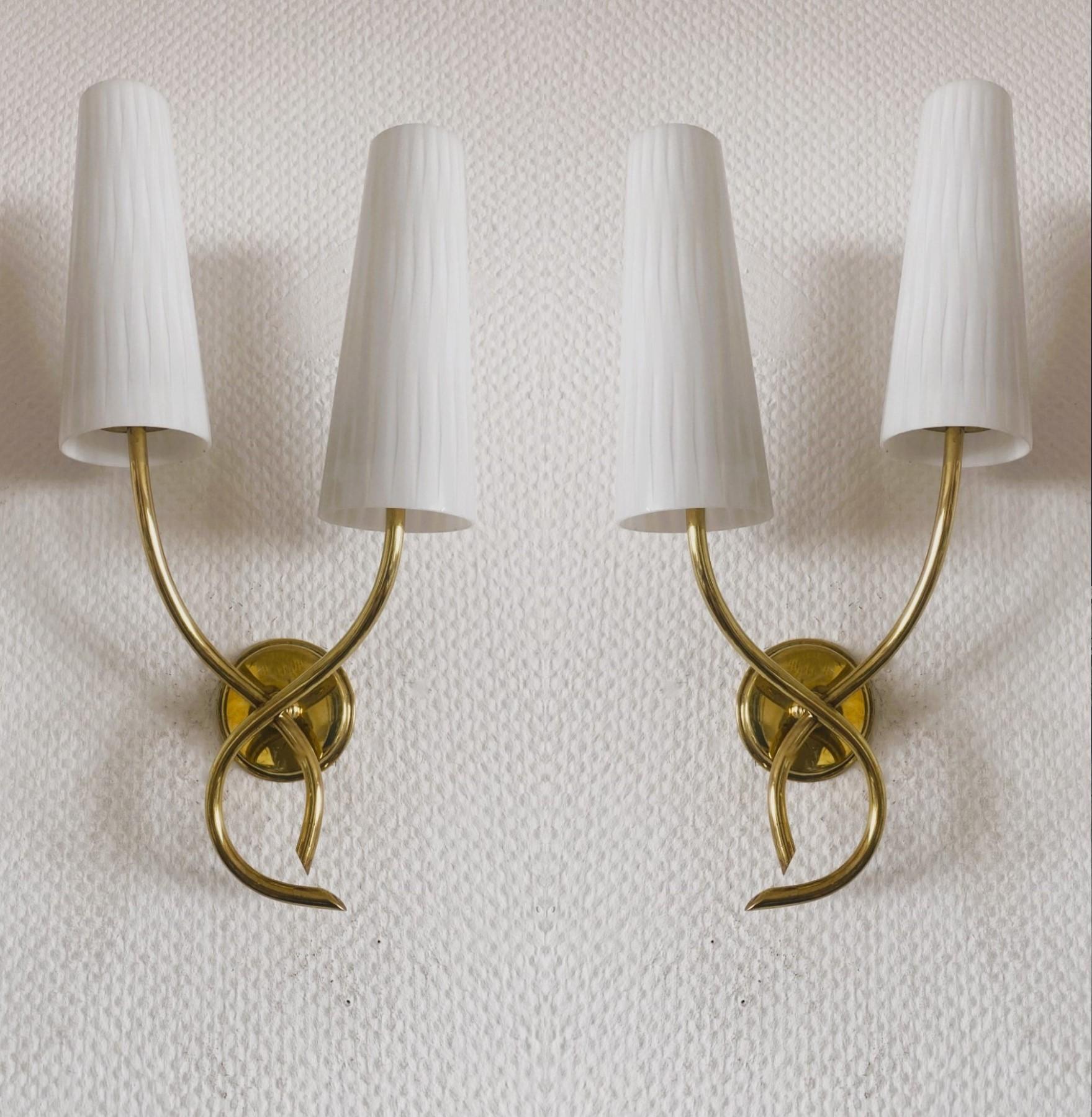 A lovely pair of Maison Lunel wall lights France, 1950s. Elegant design in gilt brass with two crossing scrolled Lamp-arm  with opaline glass shades. Both pieces in fine vintage condition, beautiful aged patina  to brass, without damages, glass