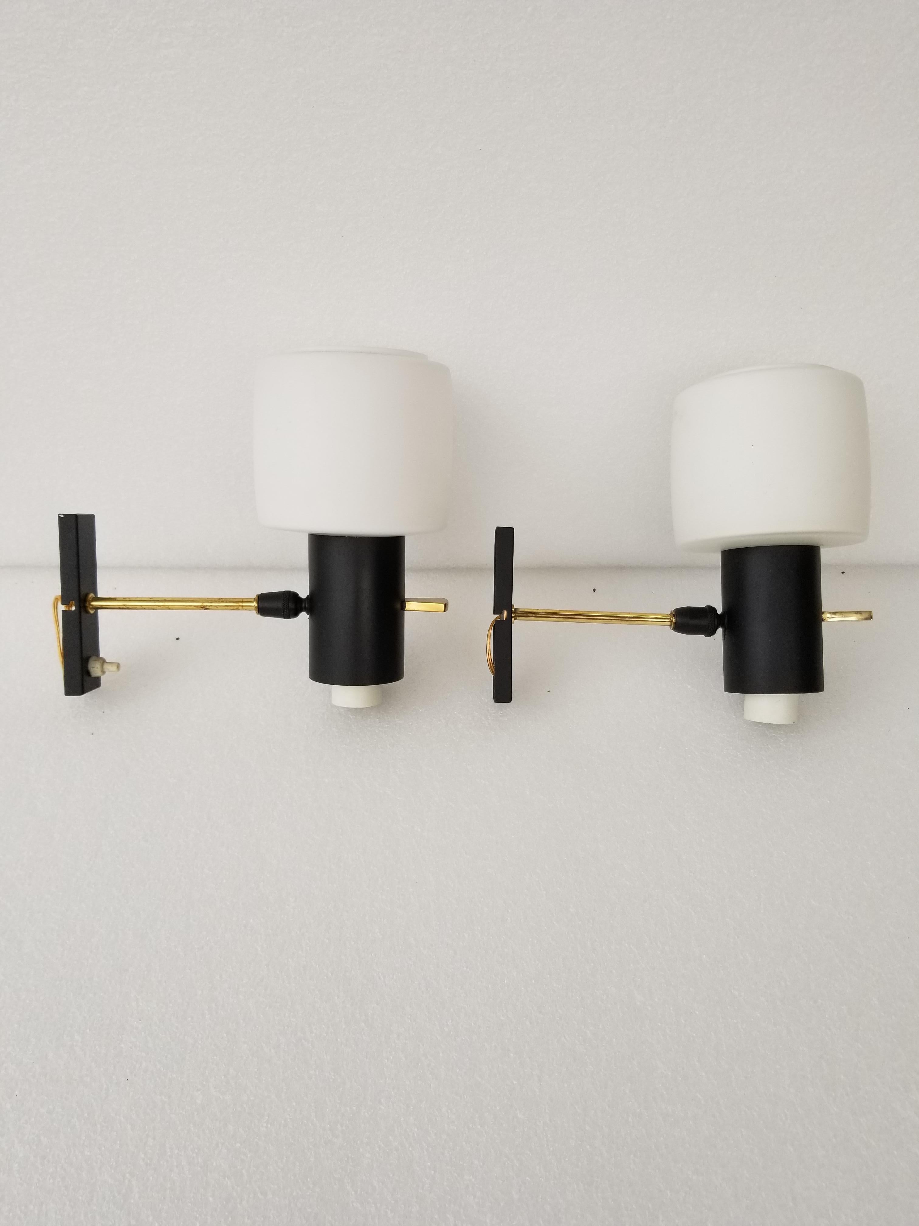 1950s pair of Maison Lunel sconces, brass and opaline glass.
Black metal back plate with brass details and white switch.
Each has a white satin glass shade.
In perfect working condition and each uses a max. 60 watts European light bulb.
   