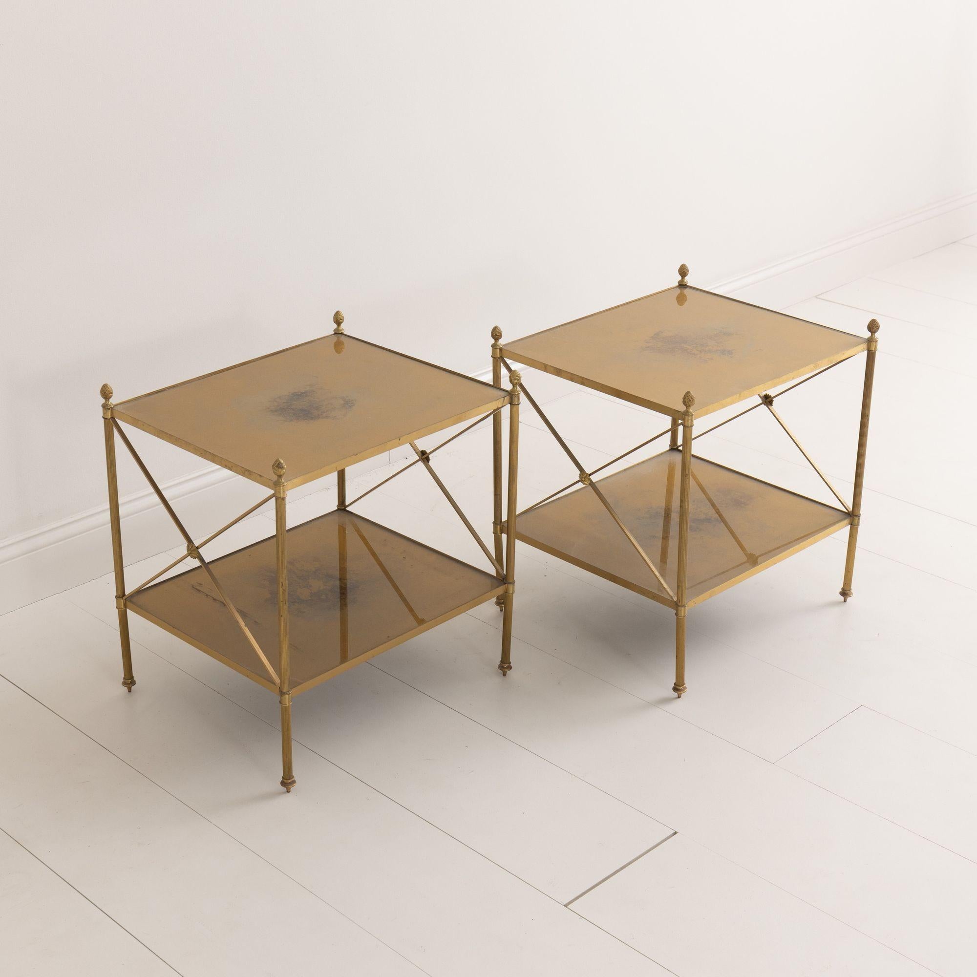 A beautiful pair of two-tiered brass side tables attributed to Maison Jansen with gold églomisé glass shelves. These neoclassical style tables have finely fluted legs with finials on each corner post and medallions on each side.  The height of the