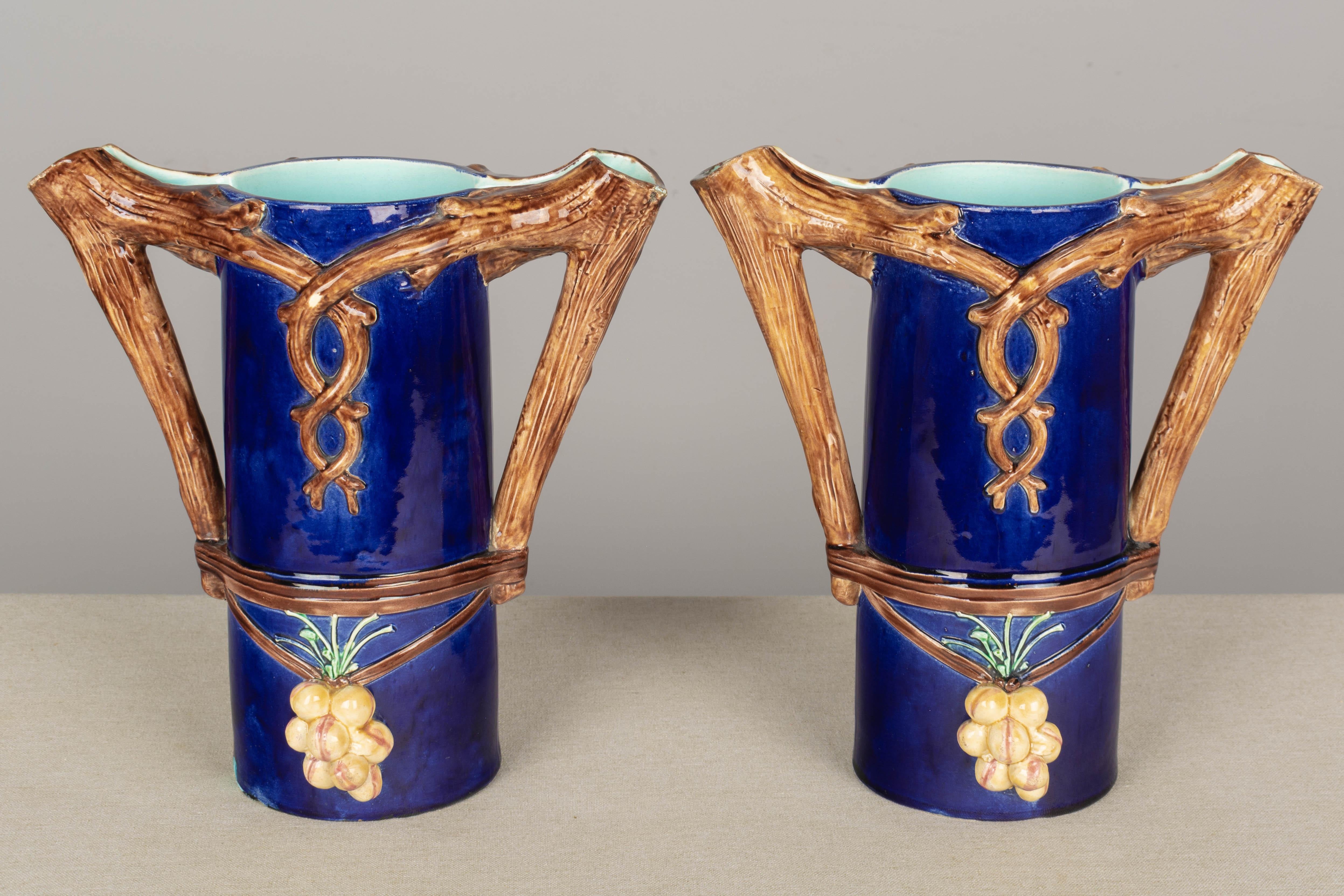 A pair of French Majolica vases or pitchers, each with double tree branch form handles and spouts. Deep, rich cobalt blue glaze with aqua interior and grape clusters. Minor glaze loss.
