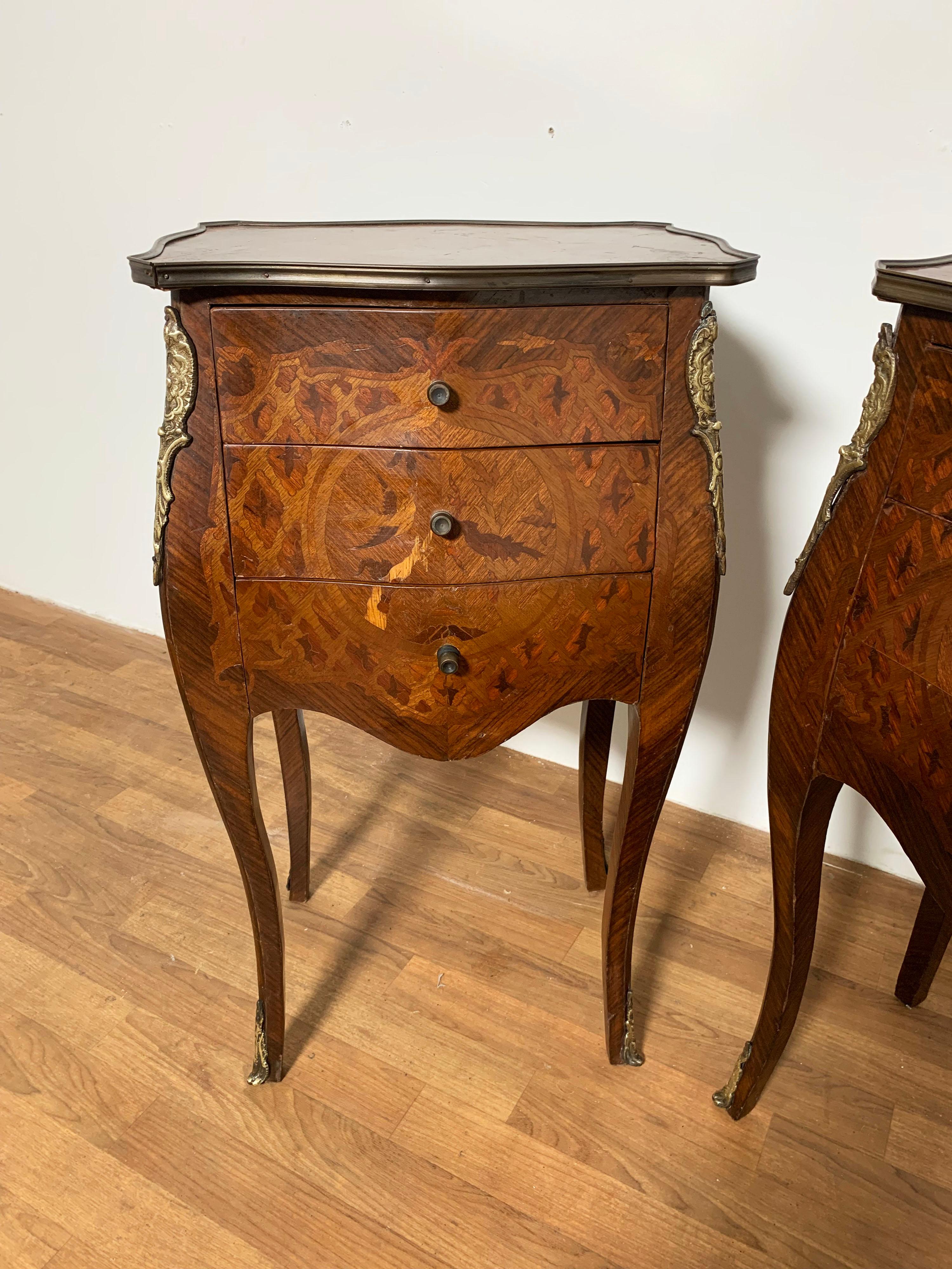A pair of petit French two drawer chests or side tables with elaborate marquetry on cabriole legs, bronze ormolu and edge banding. Would serve as nightstands well.