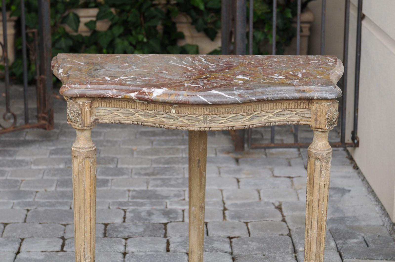 A pair of French neoclassical painted wood console tables with variegated marble tops. Born in France almost a century apart, this pair of neoclassical console tables charms our eyes with its elegant lines and distressed finish. While one was born
