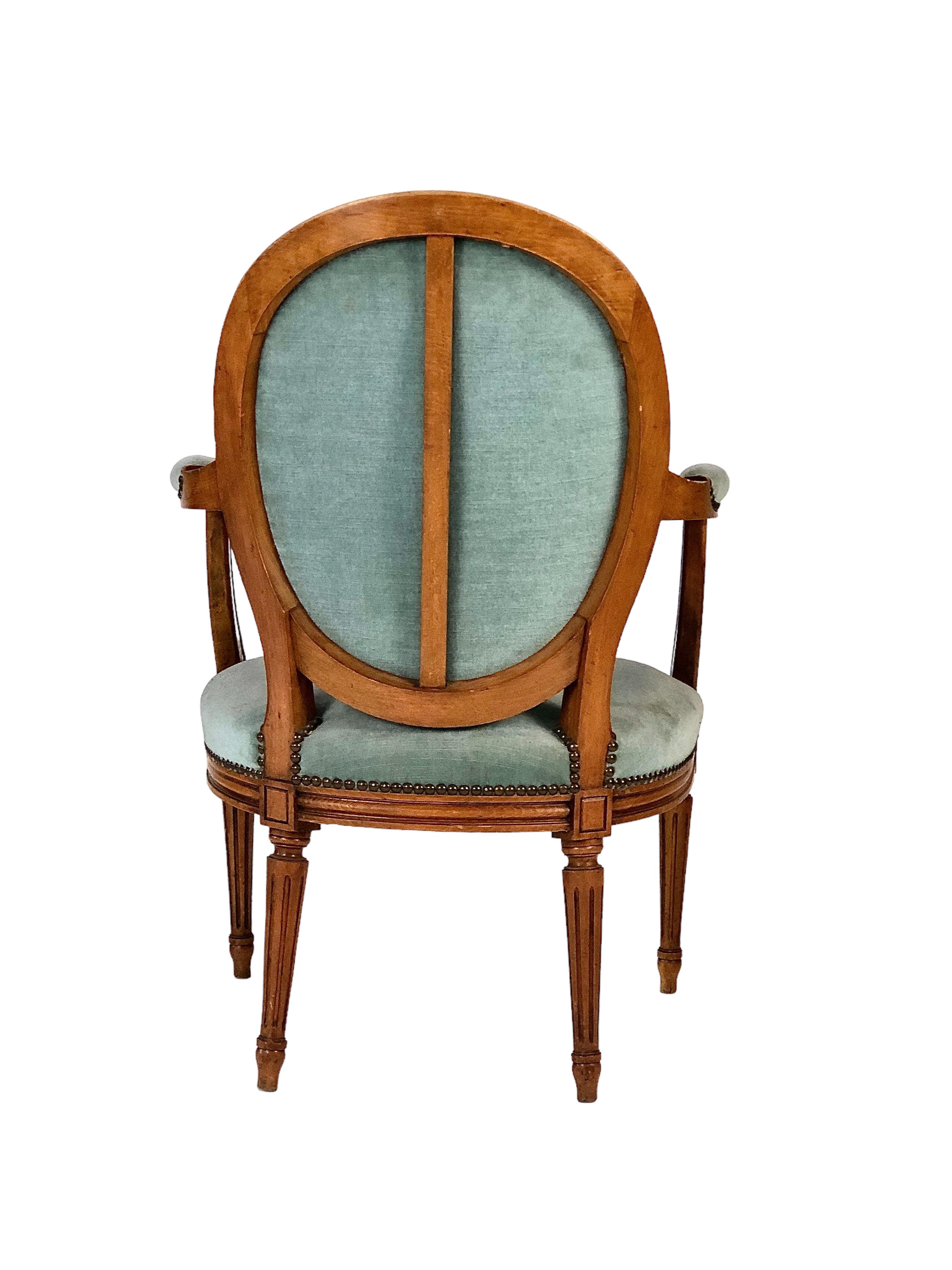 These dining armchairs are a stunning pair, made from solid chestnut and upholstered in luxurious blue velour. Each comfortable armchair boasts a padded and contoured medallion back with nailhead trim, while the tapered and fluted legs are adorned