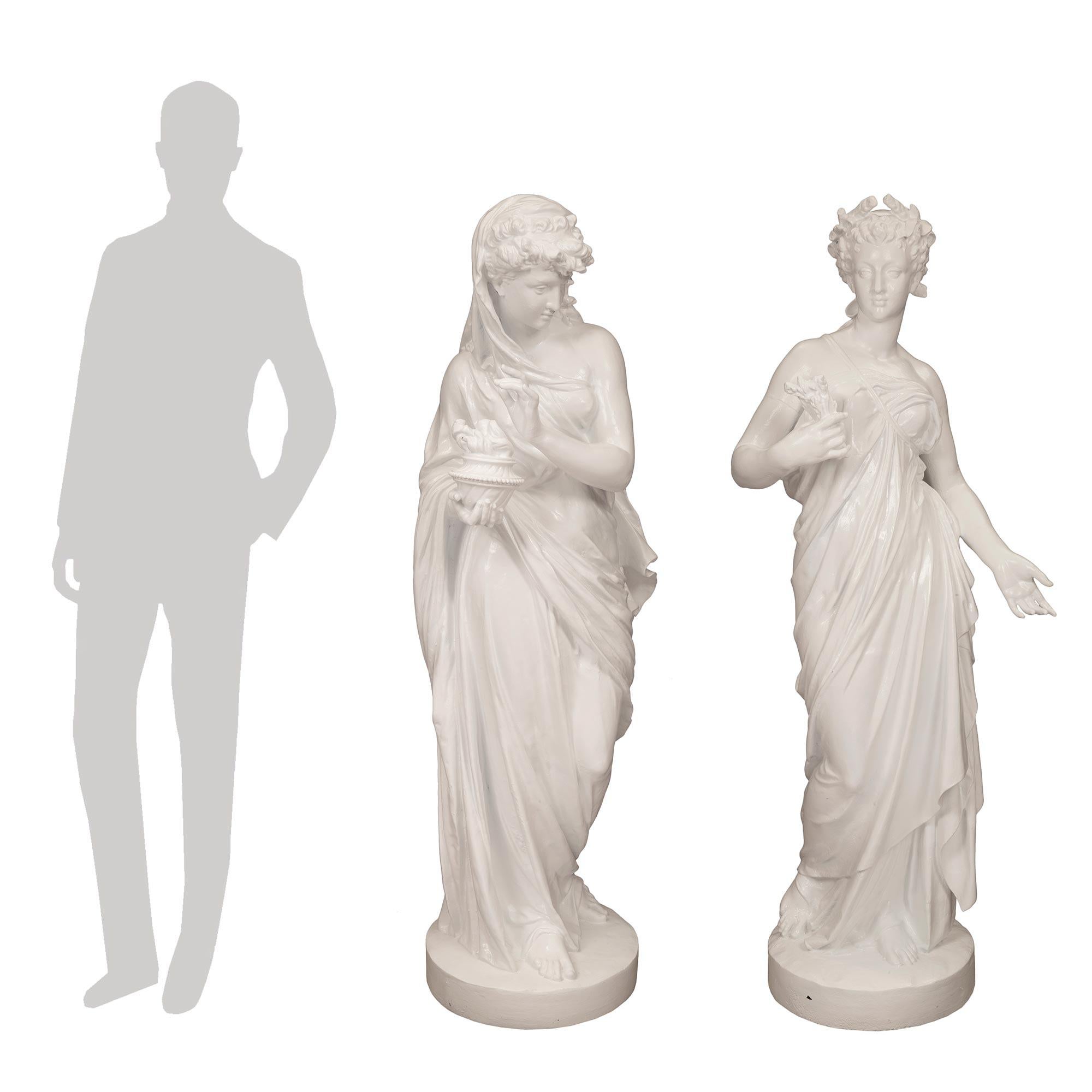 A very attractive pair of large scale French mid 19th century cast iron maidens representing summer and winter. Each maiden is draped in a classical dress, one with a head scarf holding a flaming oil lamp with a downward gaze. The other has a ribbon