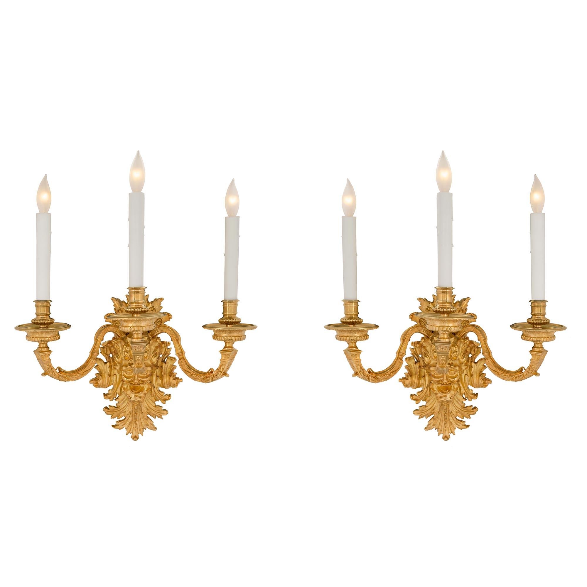 A handsome and most impressive pair of French mid 19th century Louis XIV st. ormolu three arm sconces. The sconces have a fanciful and very decorative backplate with scrolled acanthus leaves and a central masculine mask. Above the mask are the three