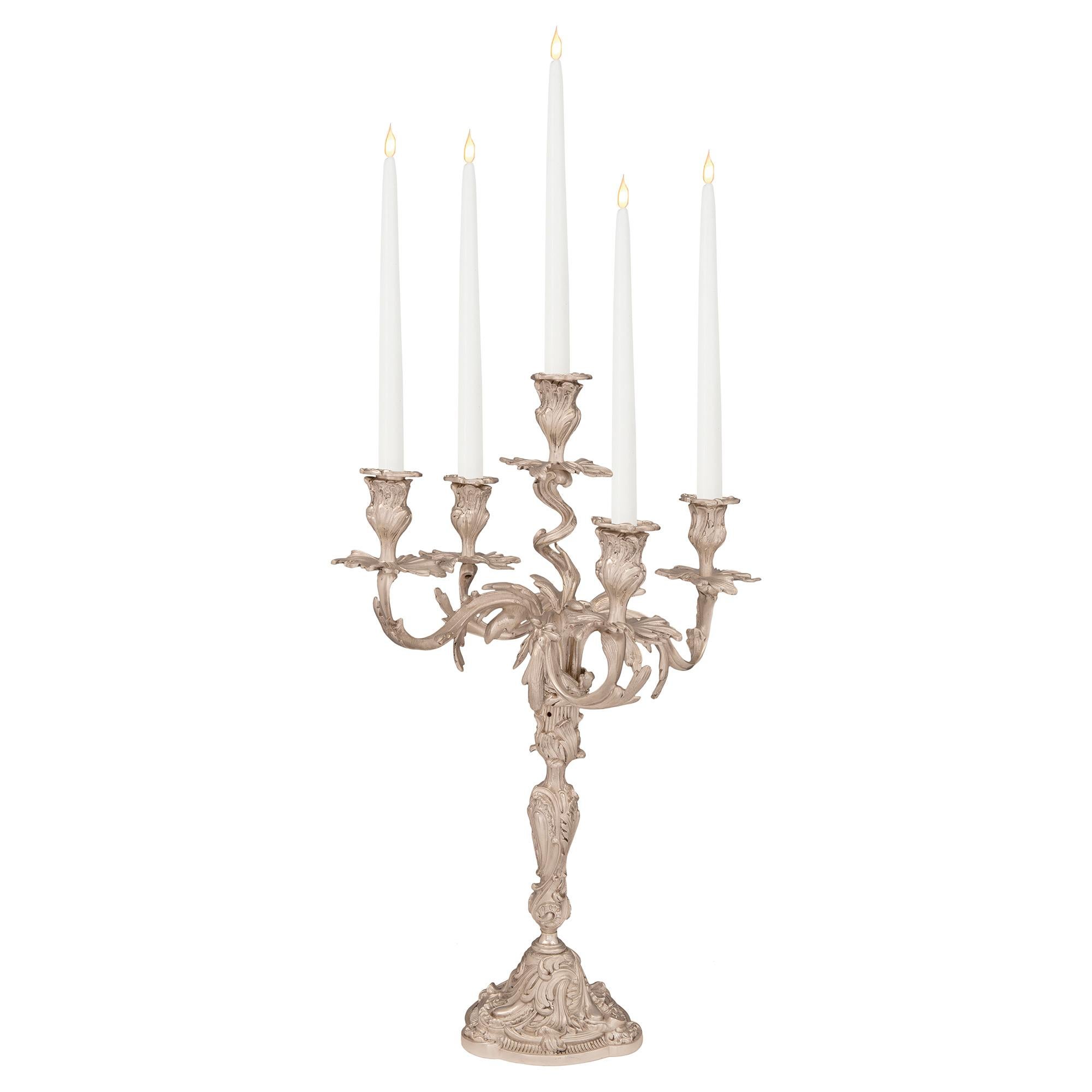 An impressive and large scaled pair of French mid 19th century Louis XV st. Silvered bronze five-arm candelabras. Each candelabra is raised by a circular base with richly chased scrolls, acanthus leaves and smooth cabochons. The central futs display