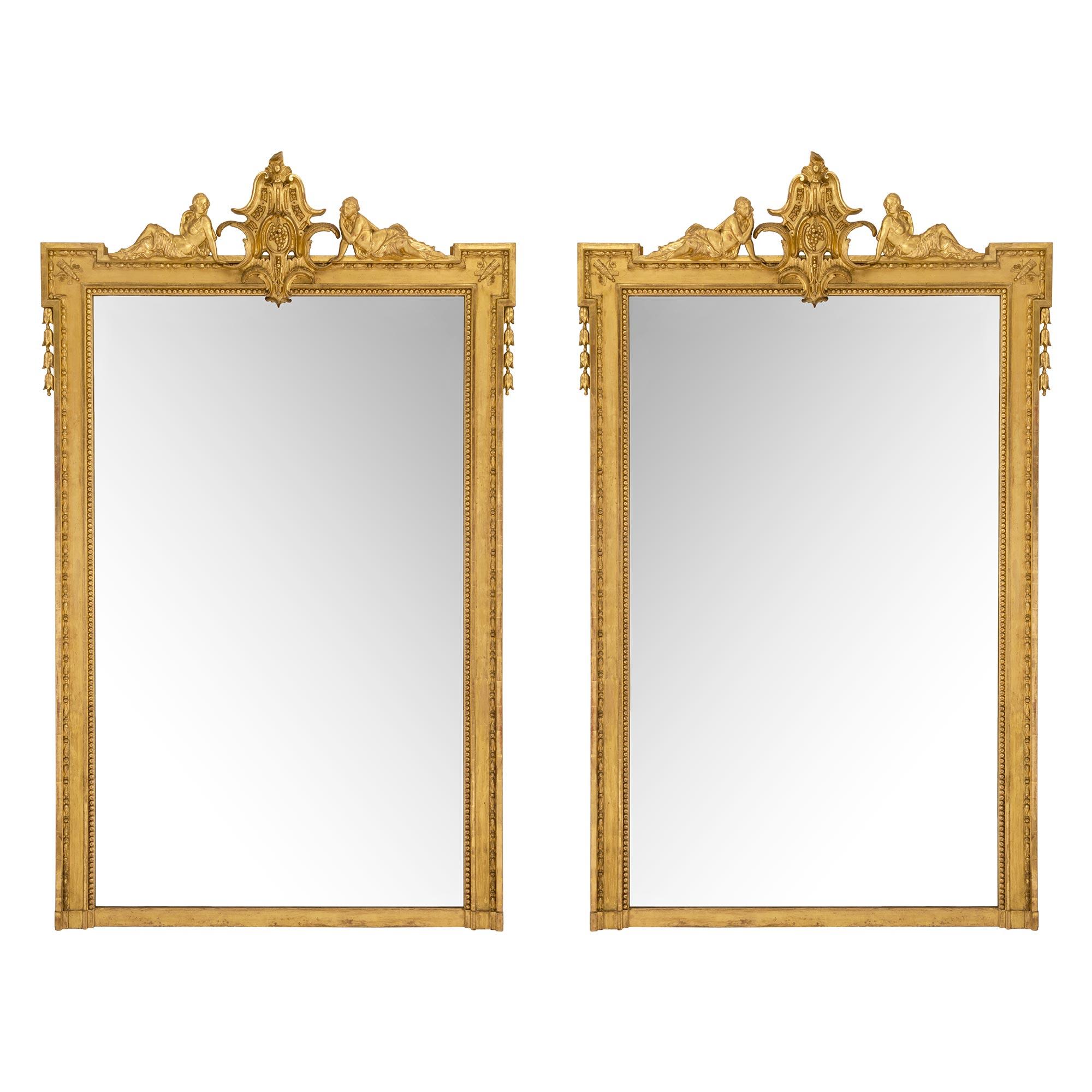 Paire impressionnante et de grande taille de miroirs en bois doré de style Louis XVI du milieu du XIXe siècle. La paire comporte un grand rang de perles à côté d'une bordure moulée avec un motif d'œuf et de fléchette. Au sommet se trouve une réserve