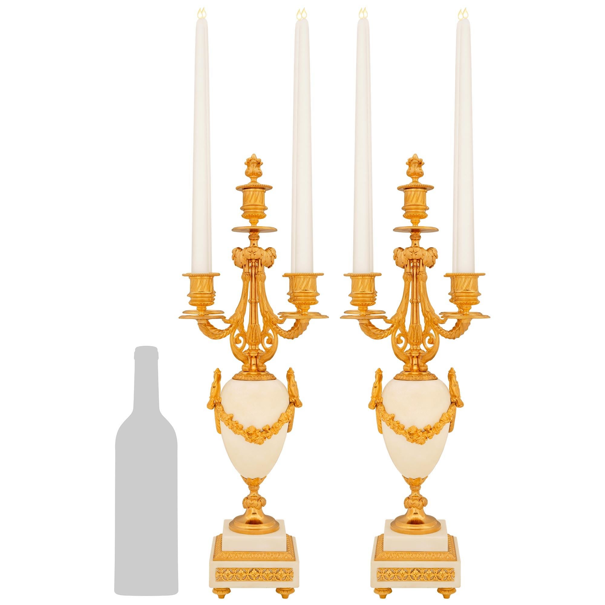 An elegant and high quality pair of French mid 19th century Louis XVI st. white Carrara marble and Ormolu candelabras. Each stunning candelabras is raised by a square marble base above four topie shaped Ormolu supports. Above is a white Carrara urn