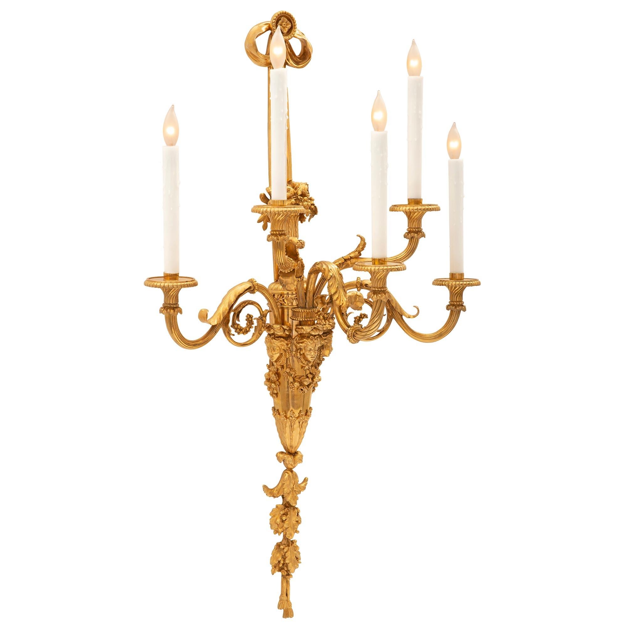 A monumental pair of French mid 19th century Louis XVI st. ormolu sconces. Each magnificent sconce has a ribbon style bow backplate accented with a rosette at the top and a cornucopia of berried flowers at the bottom. From the impressive fut extend