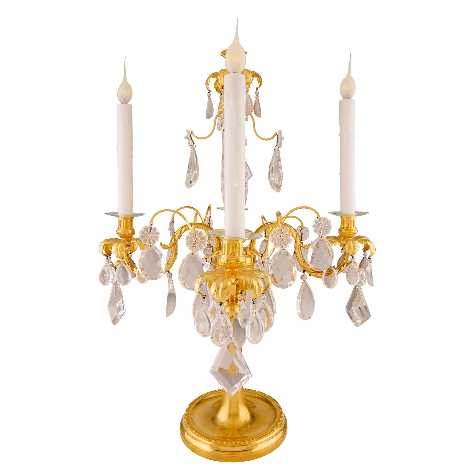 A magnificent pair of French mid 19th century Louis XVI st. ormolu and Baccarat crystal four arm girandole lamps. Each girandole is raised by an elegant circular mottled base with a mottled border and a Fine wrap around beaded band. The elegantly
