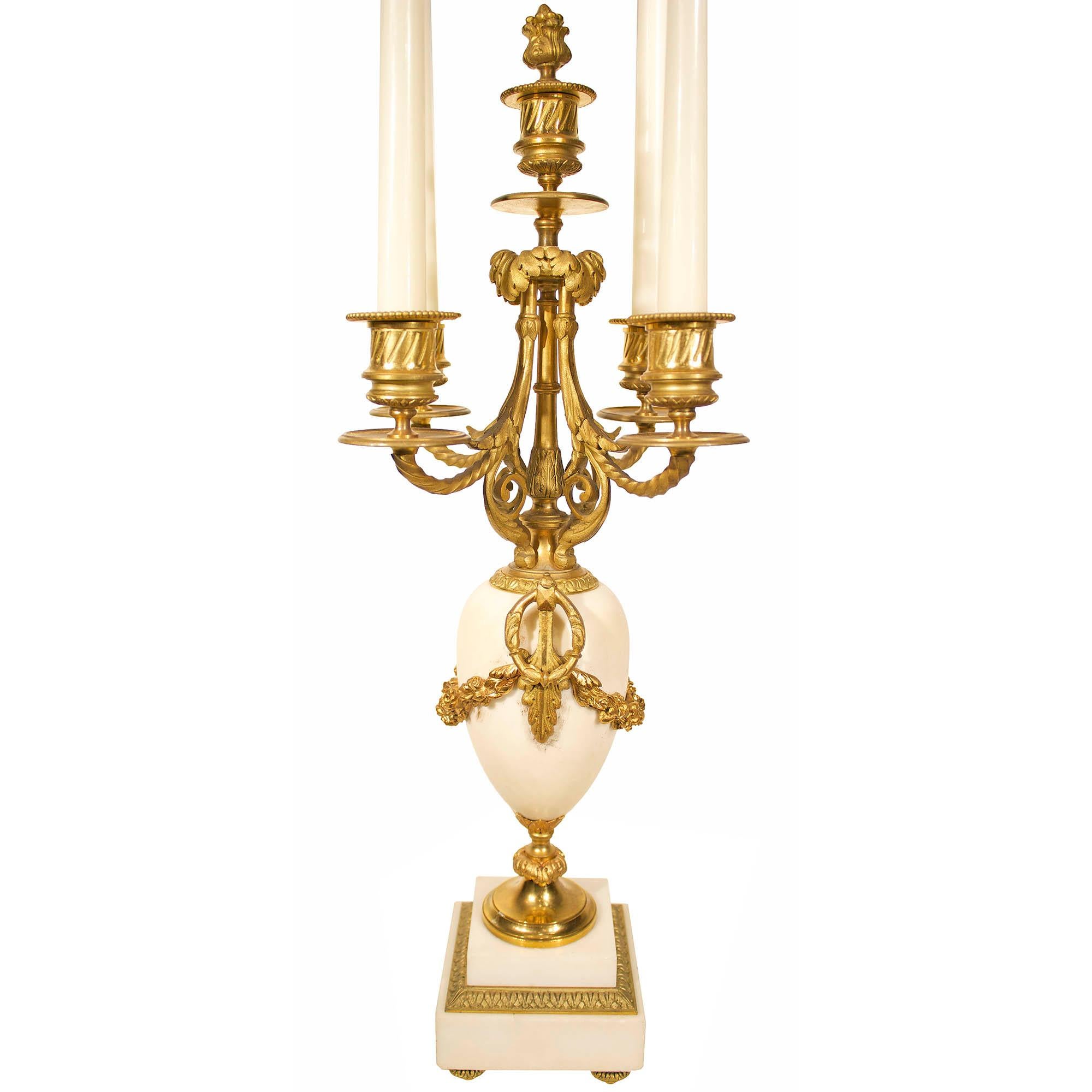 Une belle paire de candélabres français du milieu du 19ème siècle, de style Louis XVI, en marbre blanc de Carrare et bronze doré. Chacun d'eux est surélevé par une base carrée en marbre au-dessus de quatre supports en bronze ciselé et doré.