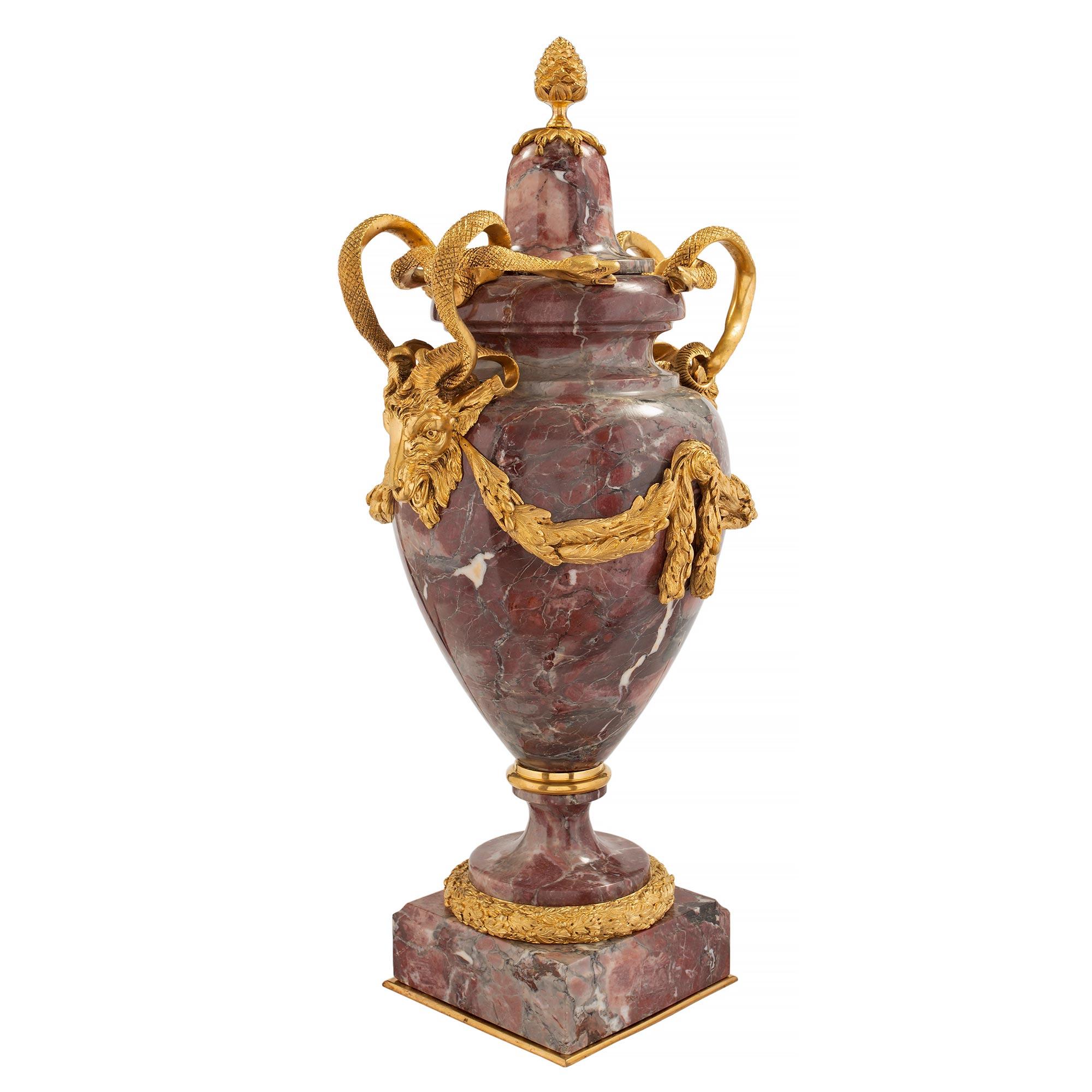 Una coppia di urne con coperchio in marmo e ormolu della metà del XIX secolo, in stile Luigi XVI. Ogni urna è sollevata da una spessa base quadrata screziata con un sottile filetto inferiore in ormolu. I piedistalli a forma di socle presentano