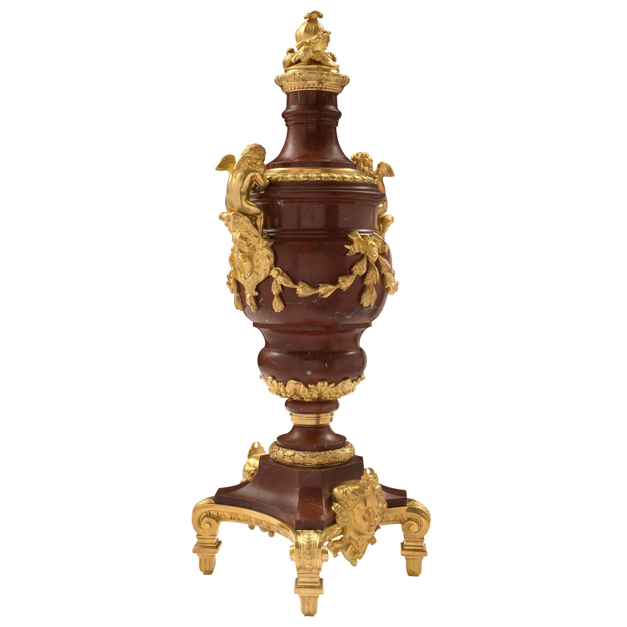 A sensational and large scale pair of French mid 19th century Louis XVI st. Rouge Antique marble and ormolu urns. Each urn is raised by an ormolu base with square feet below rich scrolls and a central richly chased female mask, repeated at the back.