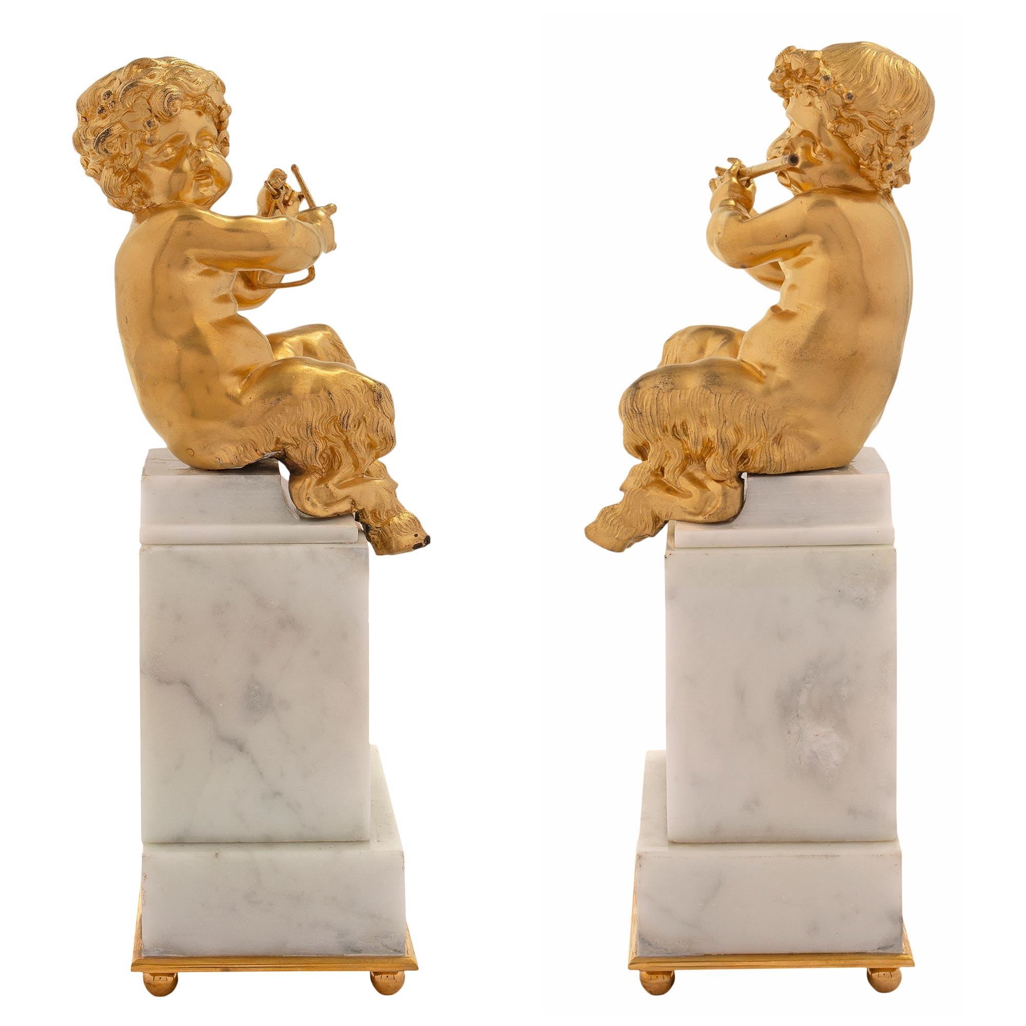 An absolutely charming pair of French mid 19th century Louis XVI st. ormolu and white Carrara marble statues of young cherubs. The pair are raised by a rectangular marble base above an ormolu socle with ball feet. One of the cherubs is playing the