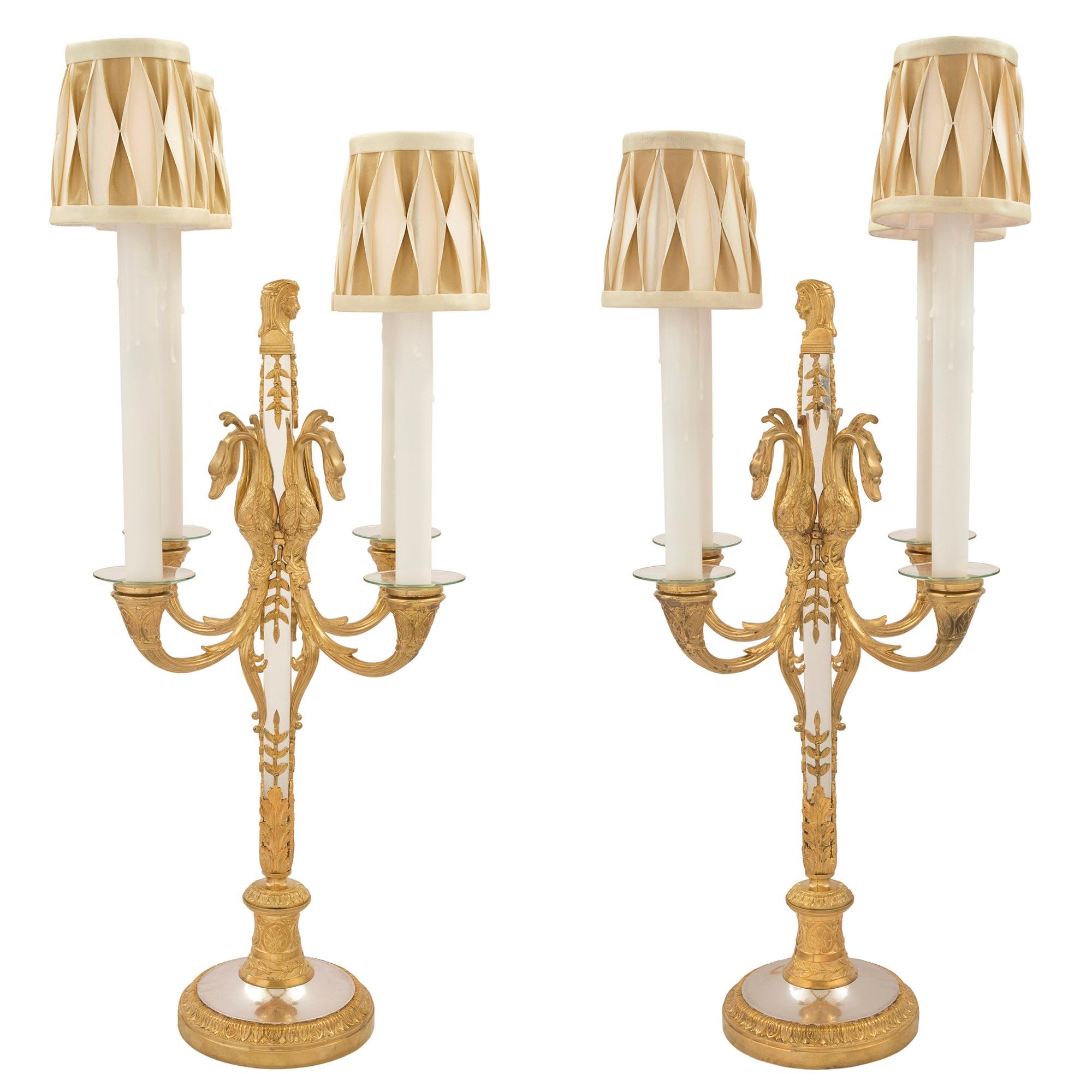 Una pareja sensacional y elegantísima de candelabros electrificados franceses de mediados del siglo XIX, de estilo neoclásico, de cuatro brazos, en bronce plateado y ormolu. La pareja se eleva sobre bases circulares de ormolina con el borde moteado