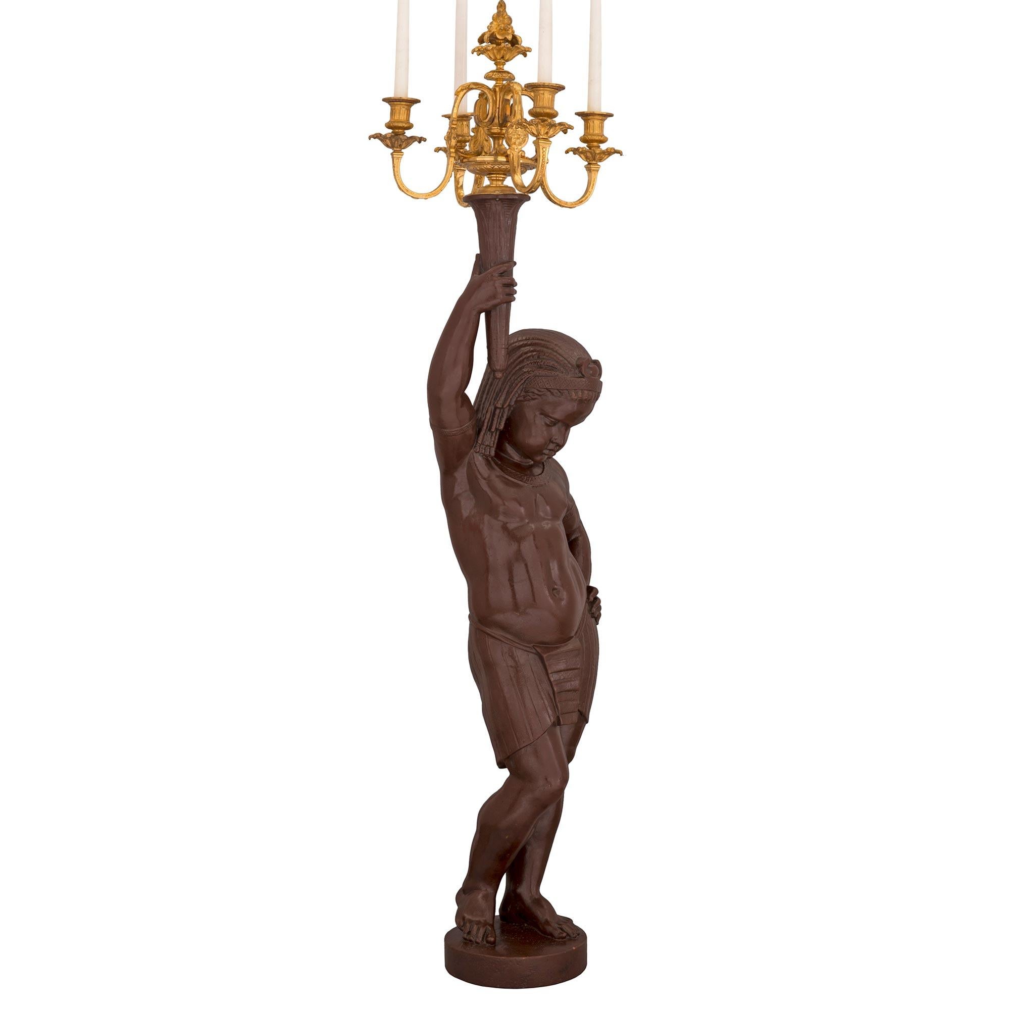 An extraordinary and large scale true pair of French mid 19th century patinated bronze and ormolu candelabra statues. Each impressive candelabra is raised by a circular base where the finely detailed figures of Nubians are standing. Each is dressed