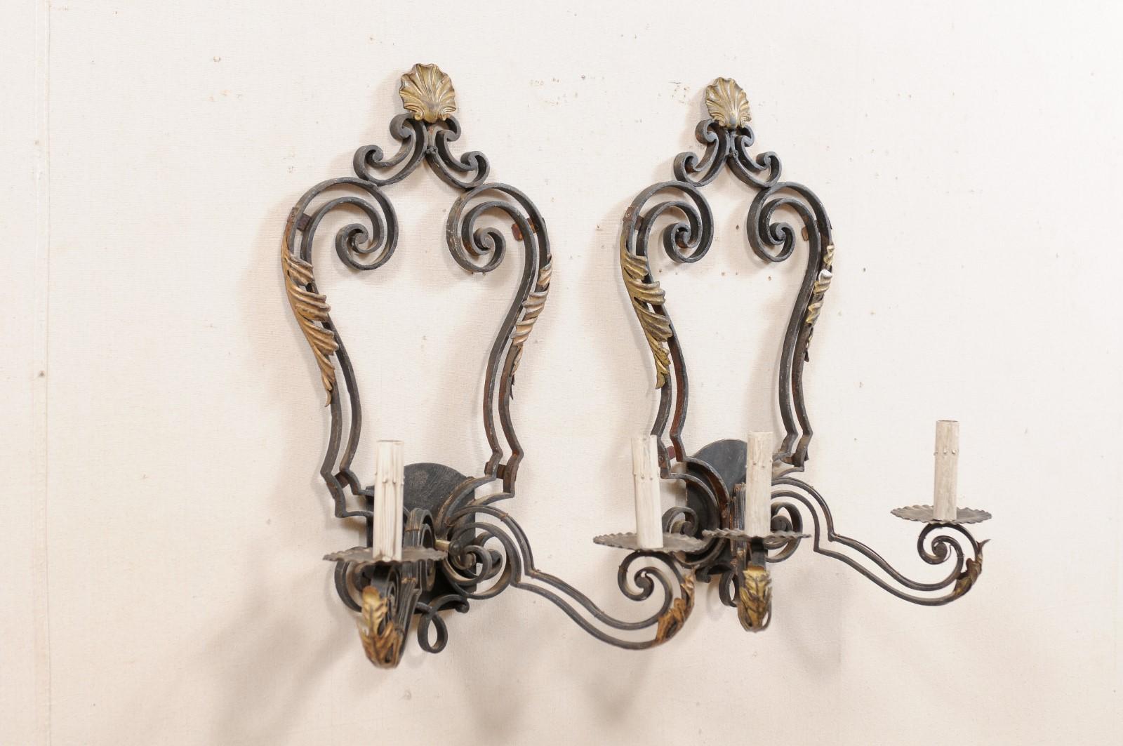 A pair of French black iron two-light sconces with gold accents from the mid-20th century. This pair of vintage French scones each have a pair of scrolling arms projecting outward, adorn with gold tone acanthus leaves, each terminate into ruffled