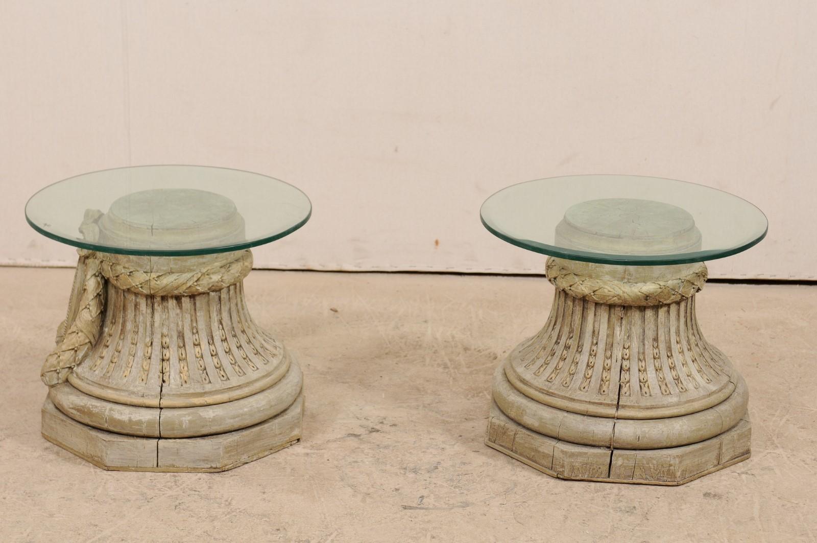A pair of French capital bases, from the early to mid-20th century, with round glass tops. This pair of small-sized coffee tables have been fashioned from a pair of French capital bases, carved with wreathed bow, fluted sides with chandelles, and an