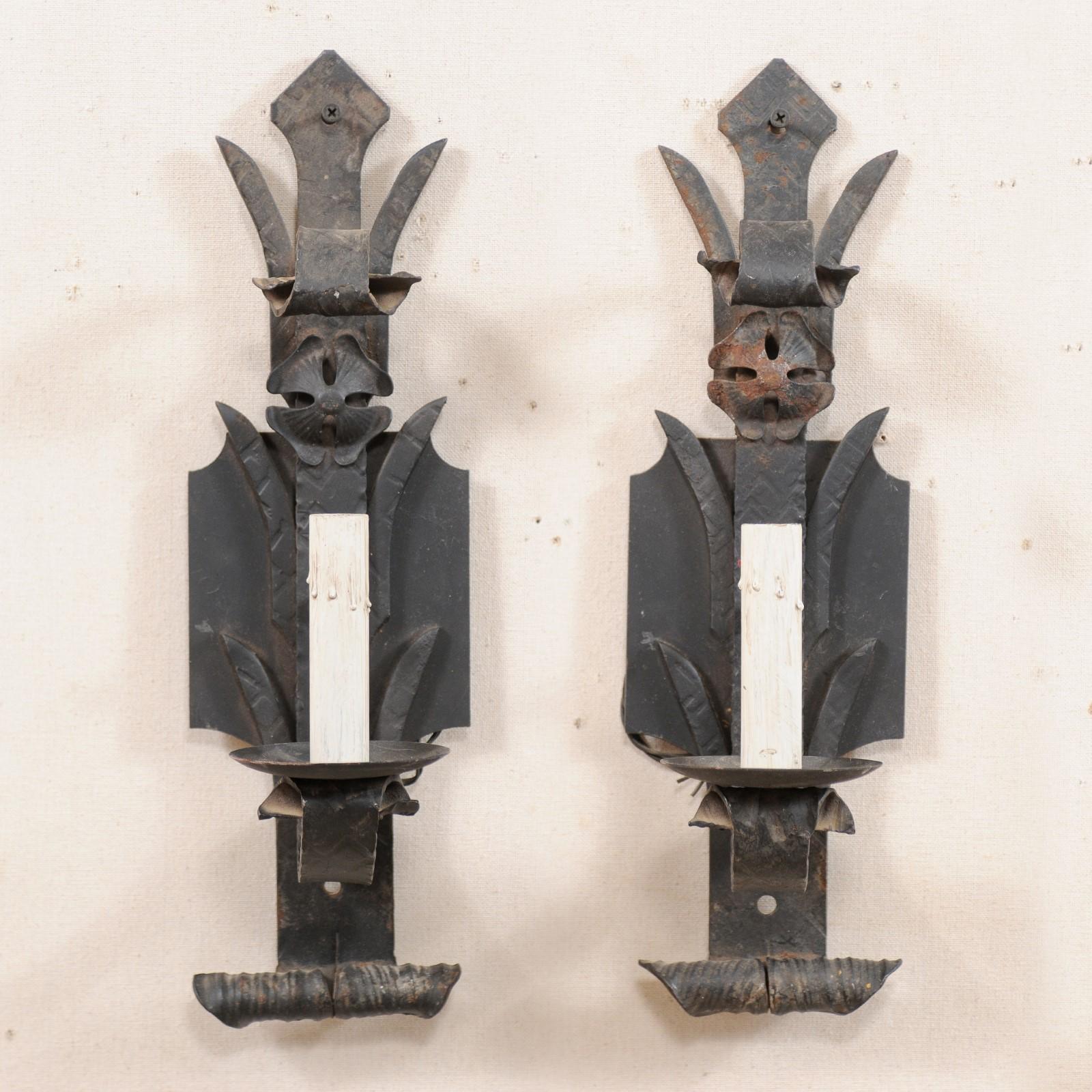 A pair of French single-light iron sconces from the mid-20th century. This vintage pair of French sconces each feature a stylized back-plate adorn with a single flower and flanked with three pair of leaves up it's post, curling out to support the