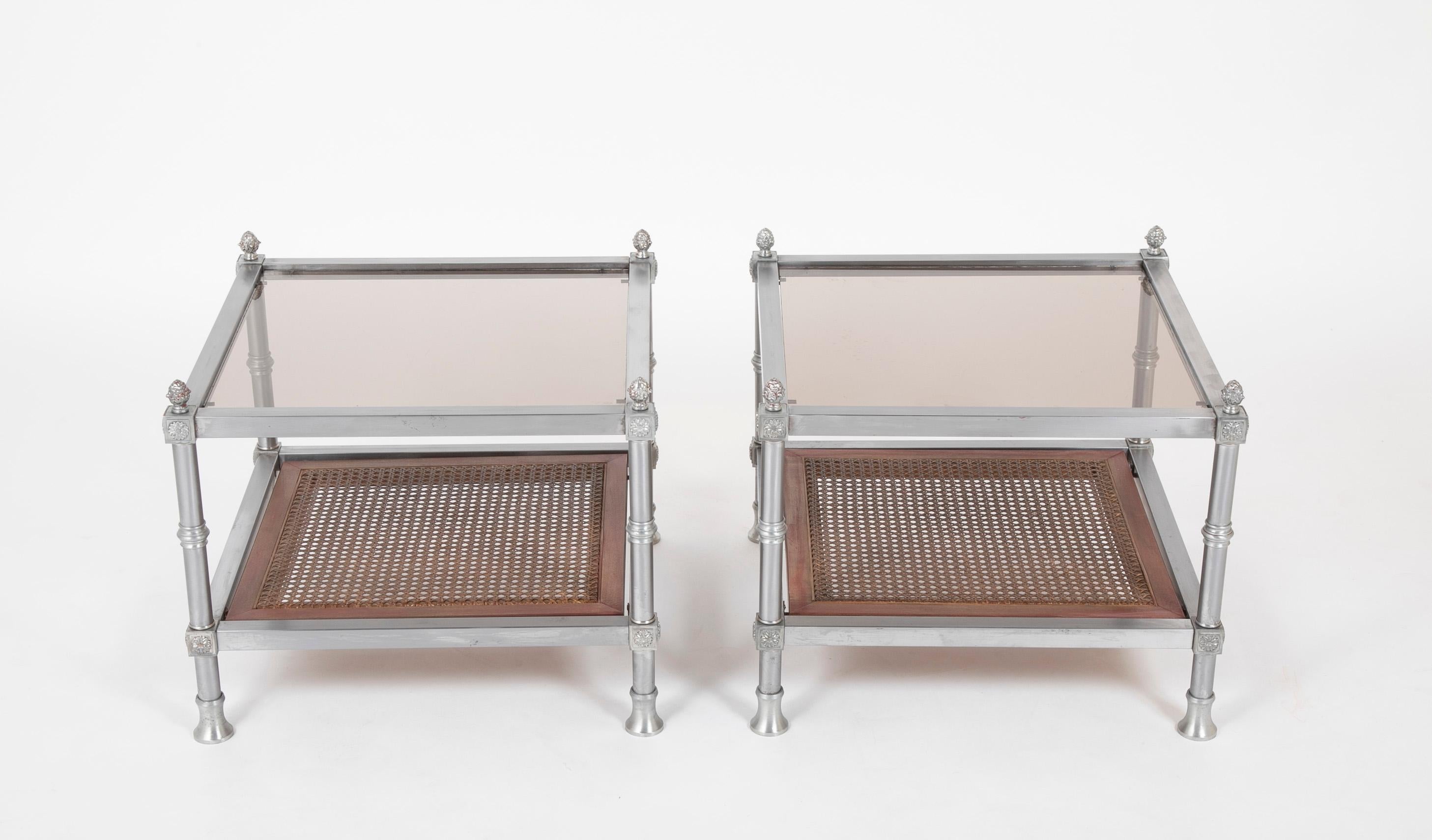 Très belle paire de tables en acier brossé de style Maison Jansen du milieu du siècle dernier avec des détails néoclassiques. Les quatre pieds sont surmontés de médaillons à fleurons et de fleurons en forme d'ananas. Plateau en verre teinté avec