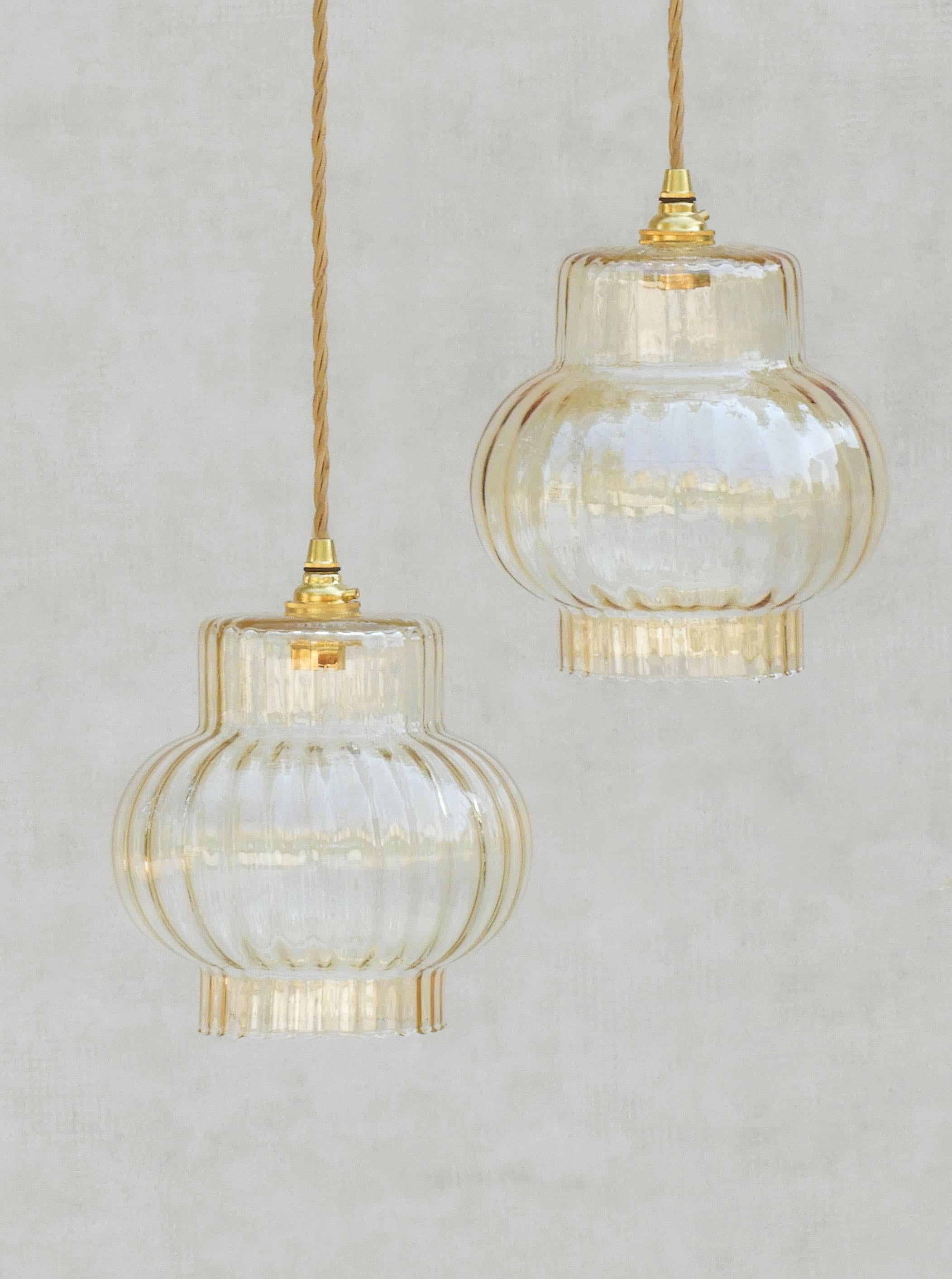 A pair of fluted champagne-coloured glass pendant lights from mid-century France.
Two ribbed blown glass shades in subtle golden amber. 
Stylish and versatile these pendant lights can be hung grouped or individually and would be ideal as suspended