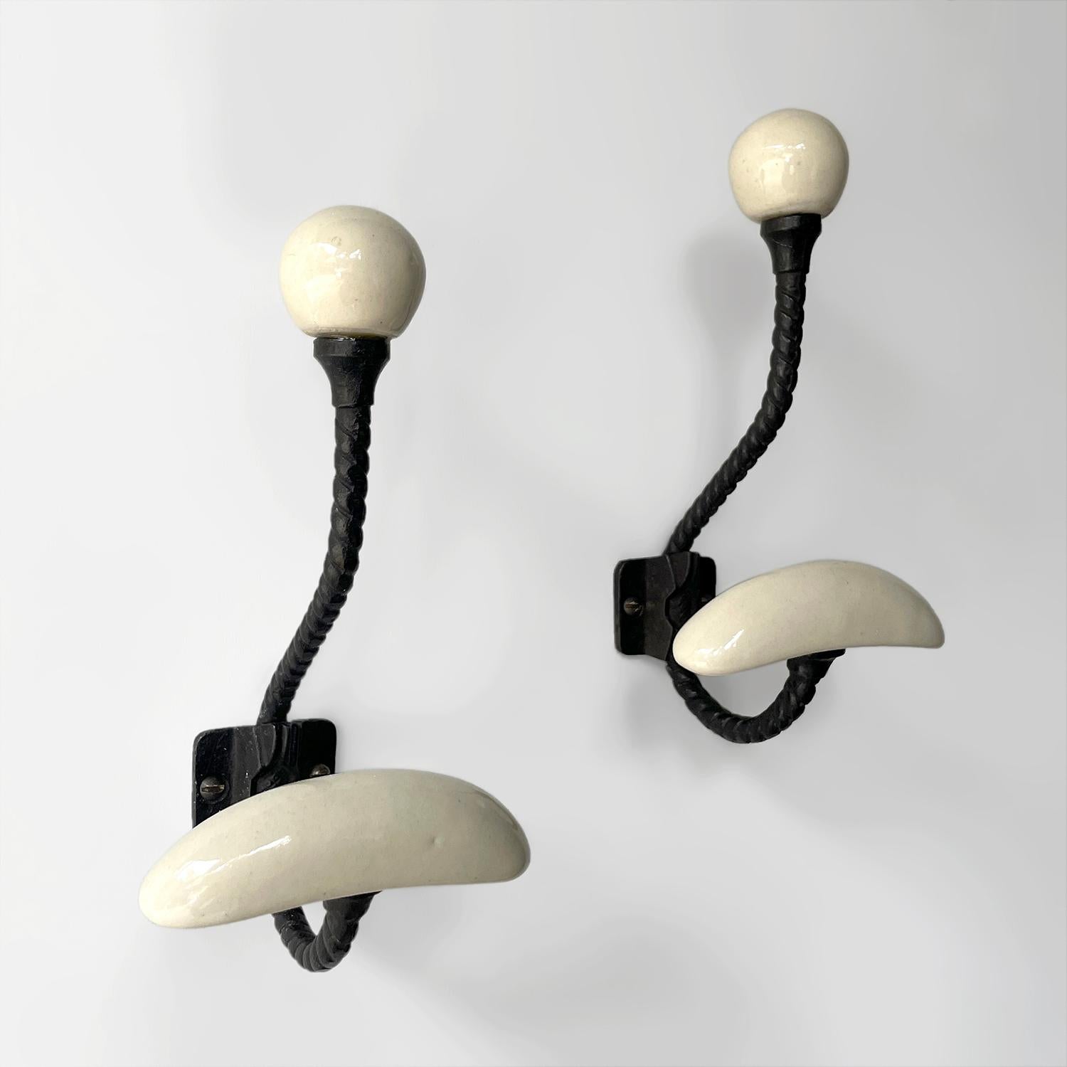 Pair of French porcelain & iron hooks
France, mid century 
Each hook provides plenty of storage 
The frames are made of twisted iron and finished with a porcelain upper ball hook as well as a lower  arched wide panel hook 
Each wall mounted hook is