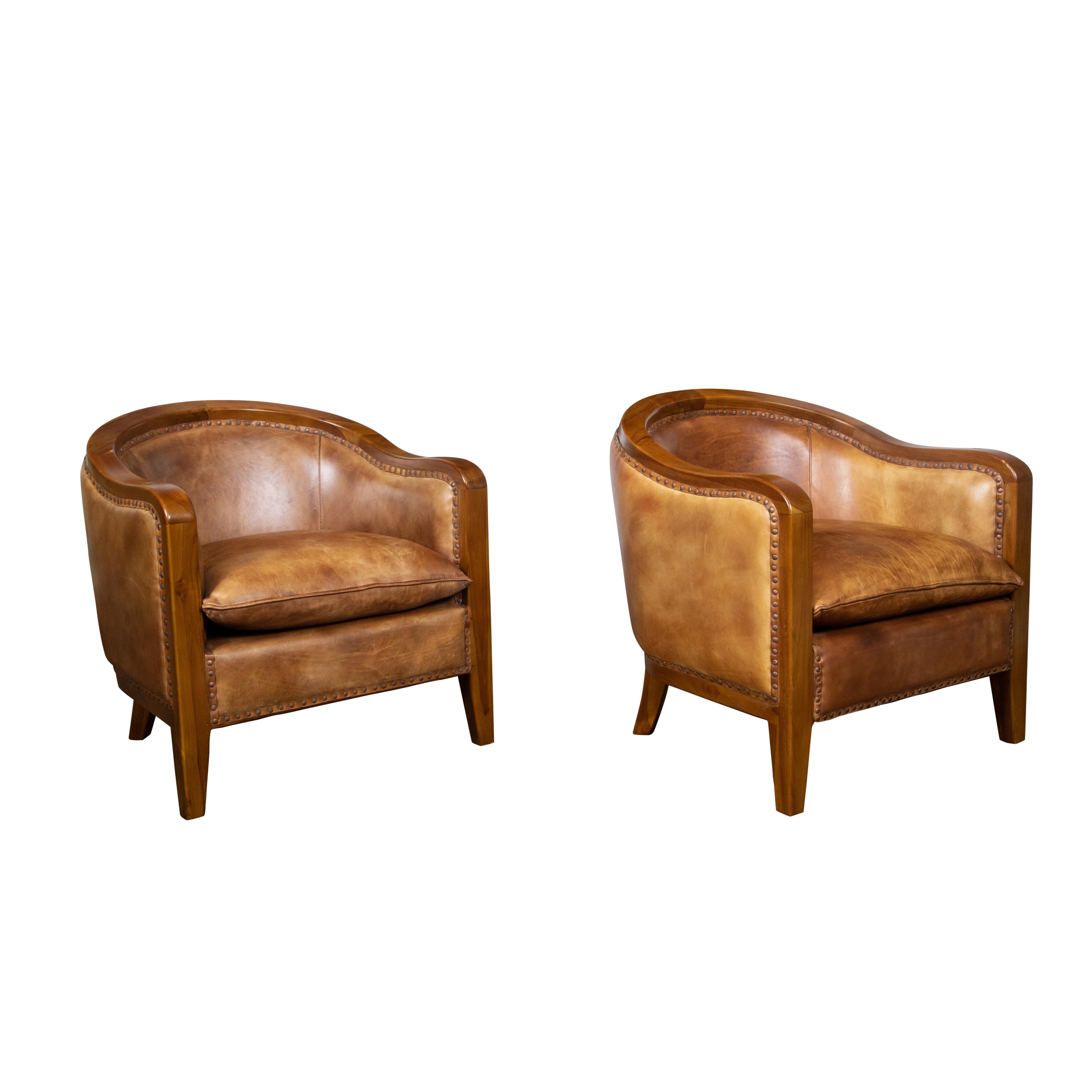 A pair of French vintage wood and brown leather horseshoe club chairs from the mid 20th century, with ornate nailhead trim and tapered legs. Created in France during the Midcentury period, this pair of club chairs charms us with its simple yet