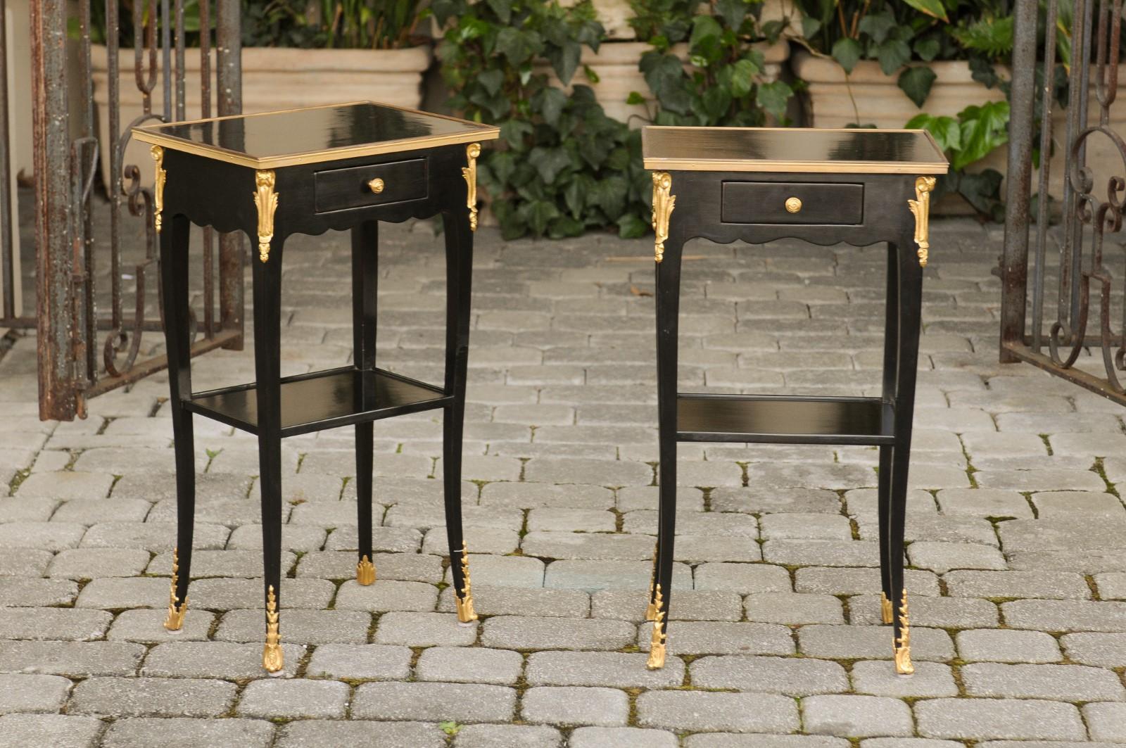 A vintage pair of French ebonized bedside tables from the mid-20th century, with ormolu décor, single drawer and lower shelf. Born in France during the midcentury period, each of this pair of bedside tables features a rectangular top surrounded by a