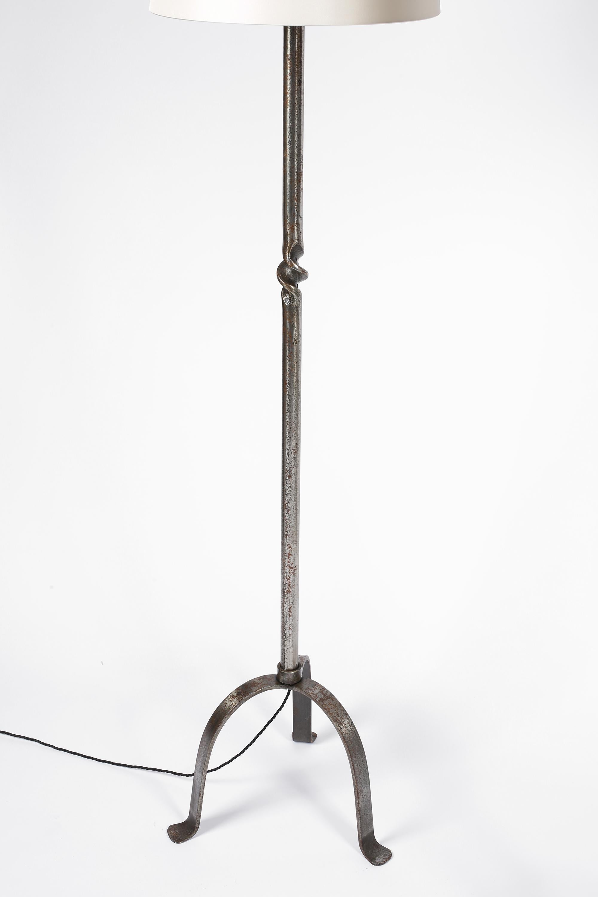 Sold separately.

A pair of simple forged iron floor lamps with subtle torsade detailing to the stems and curved three point bases. The pair differing only in patination to the ironwork. French, c. 1950s. Supplied with off-white dupion silk shades.
