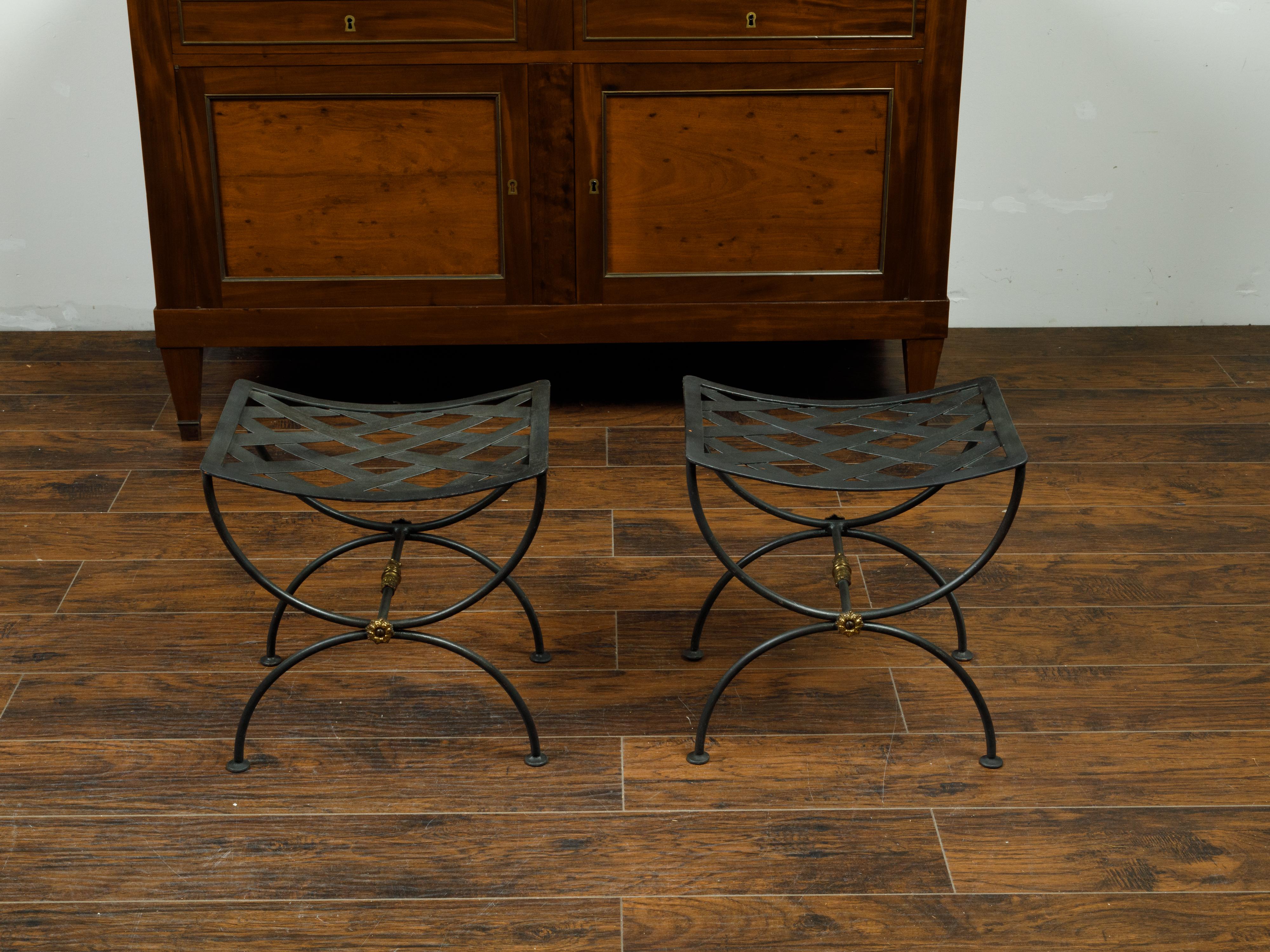 A pair of French vintage iron curule stools from the mid 20th century, with latticed tops and X-form bases. Created in France during the midcentury period, each of this pair of iron stools features a curving latticed top sitting above a double