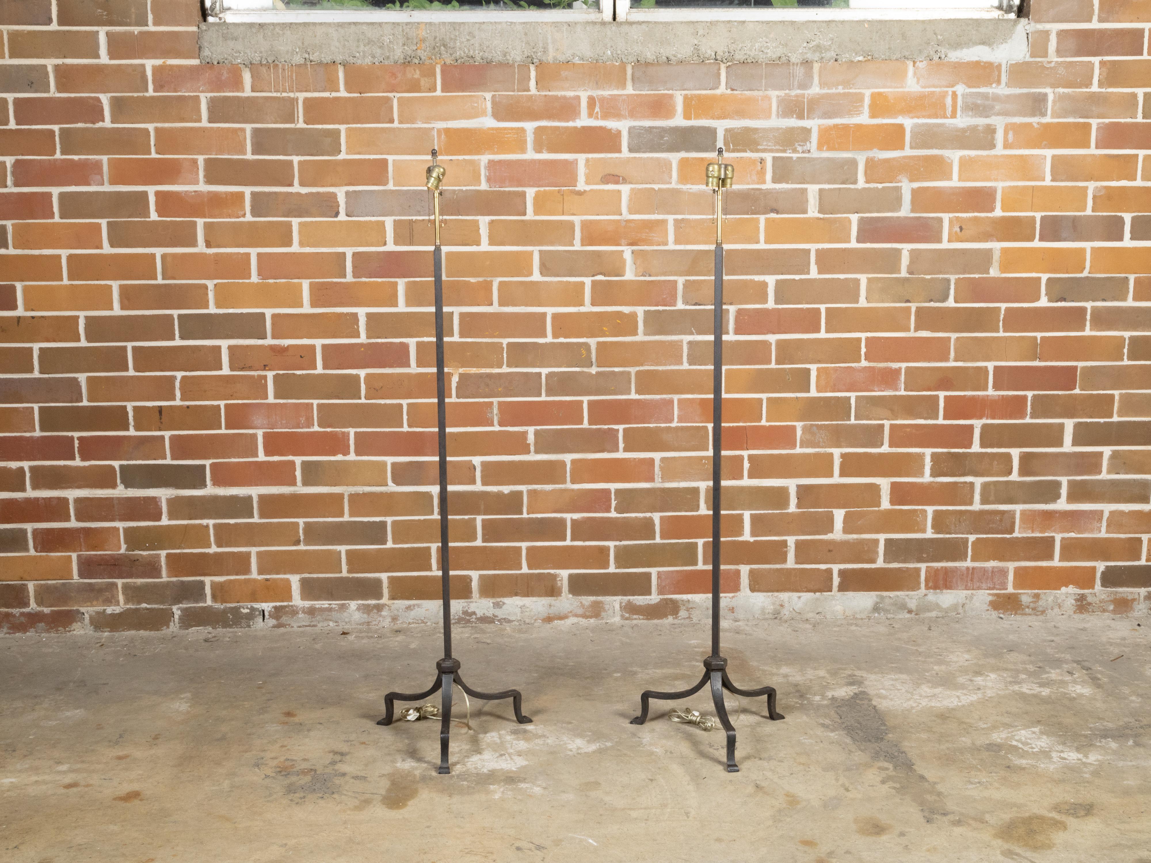 A pair of vintage French iron two-light floor lamps from the mid 20th century, with cluster sockets, tripod bases and scrolling feet. Created in France during the Midcentury period, each of this pair of iron floor lamps features a central shaft