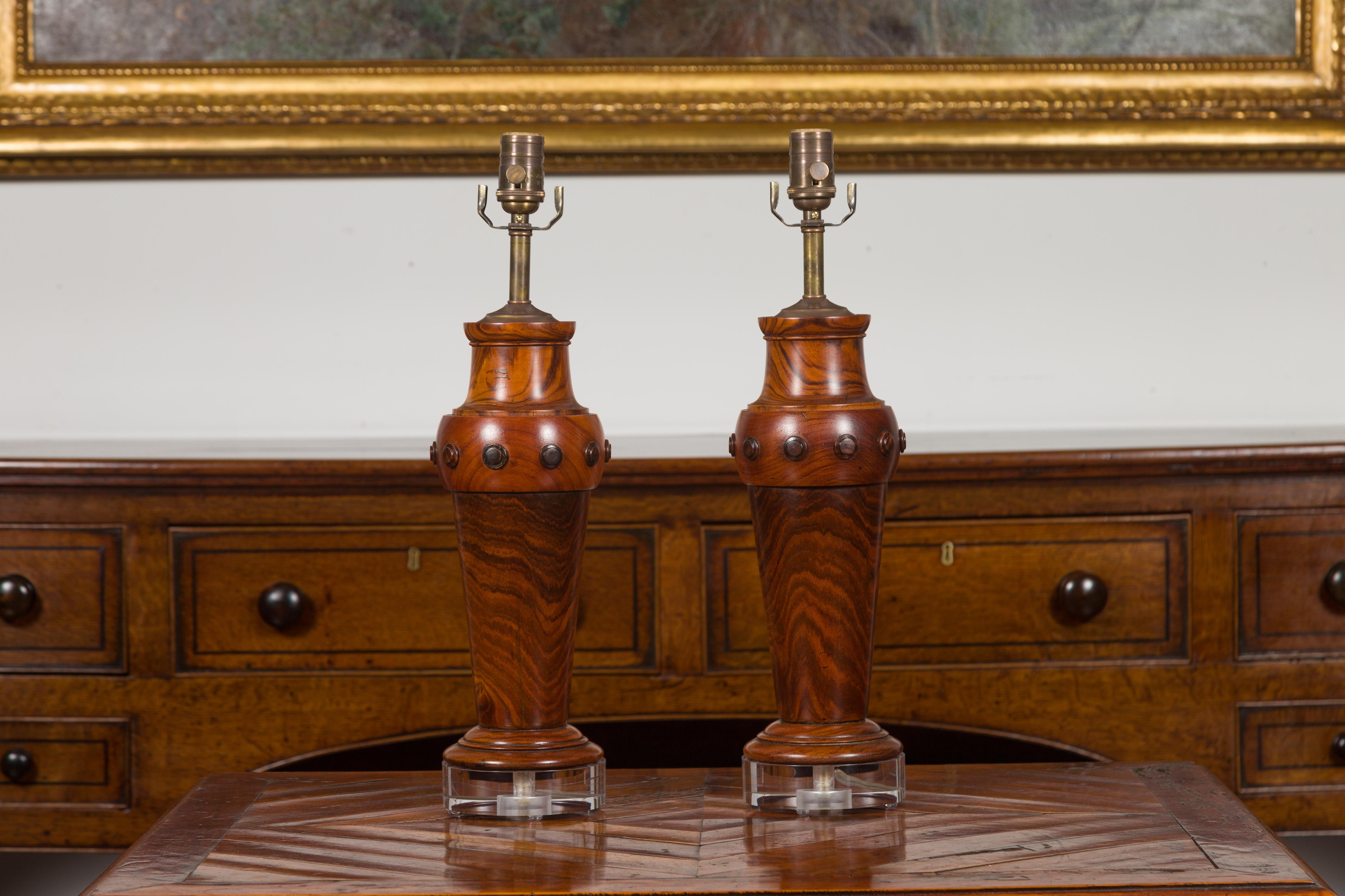 A pair of French turned wood table lamps from the mid-20th century with Lucite bases. Created in France during the midcentury period, each of this pair of table lamps attracts our attention with its beautiful wood grain and medallion accentuation.