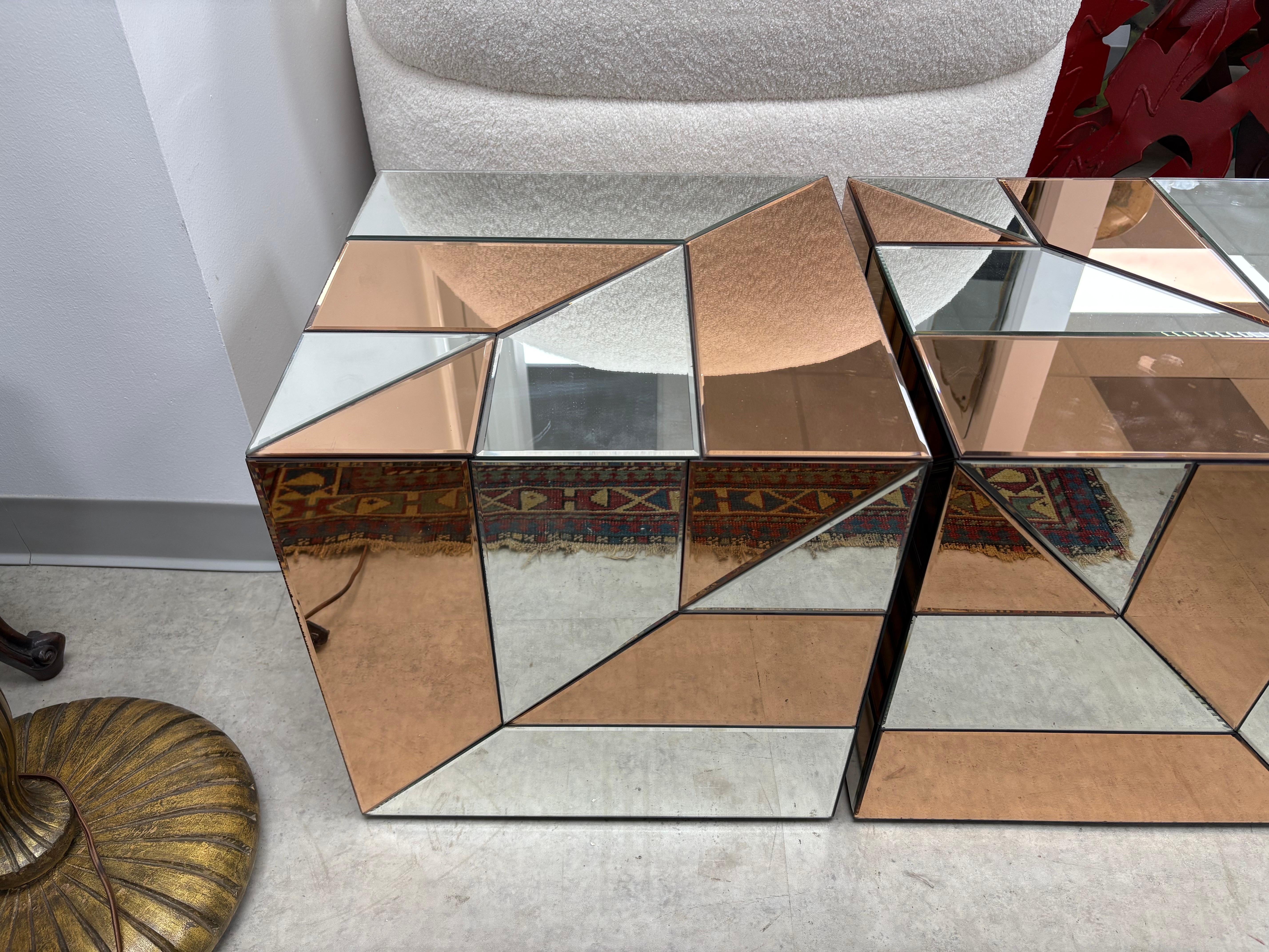 Paire de tables cubiques modernes en miroir.
Nous vous proposons une paire de tables cubiques en miroir ou de piédestaux de style Art Déco français.  panneaux de miroir biseauté alternant des applications géométriques en argent et en rose.