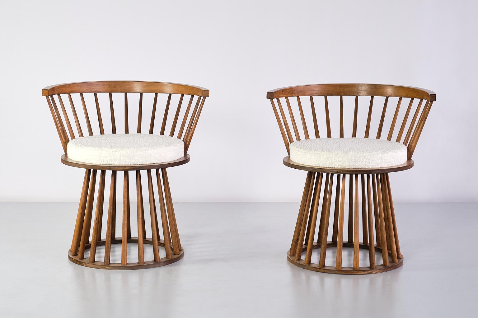 This striking pair of armchairs was produced in France in the late 1950s. The design is marked by the embracing, curved spindle back. The circular spindle base with the its upwards tapering wooden bars is giving the chairs a distinct and dynamic