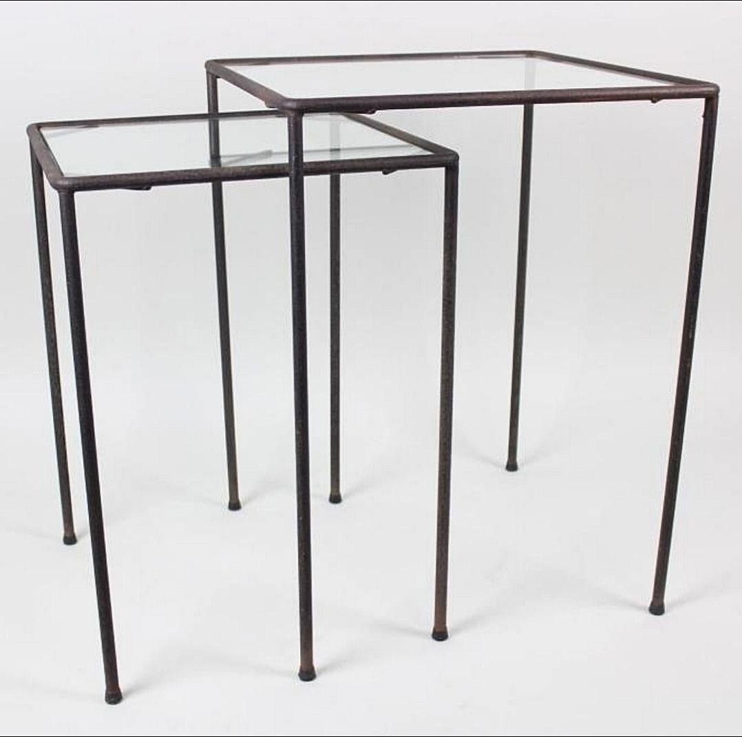 This is a very clean modernist pair of occasional tables that happen to also be nesting tables . The iron is hand wrought and pieced together to create these frames . Retaining the original small rubber stoppers on the bottom of the feet. 
Smaller