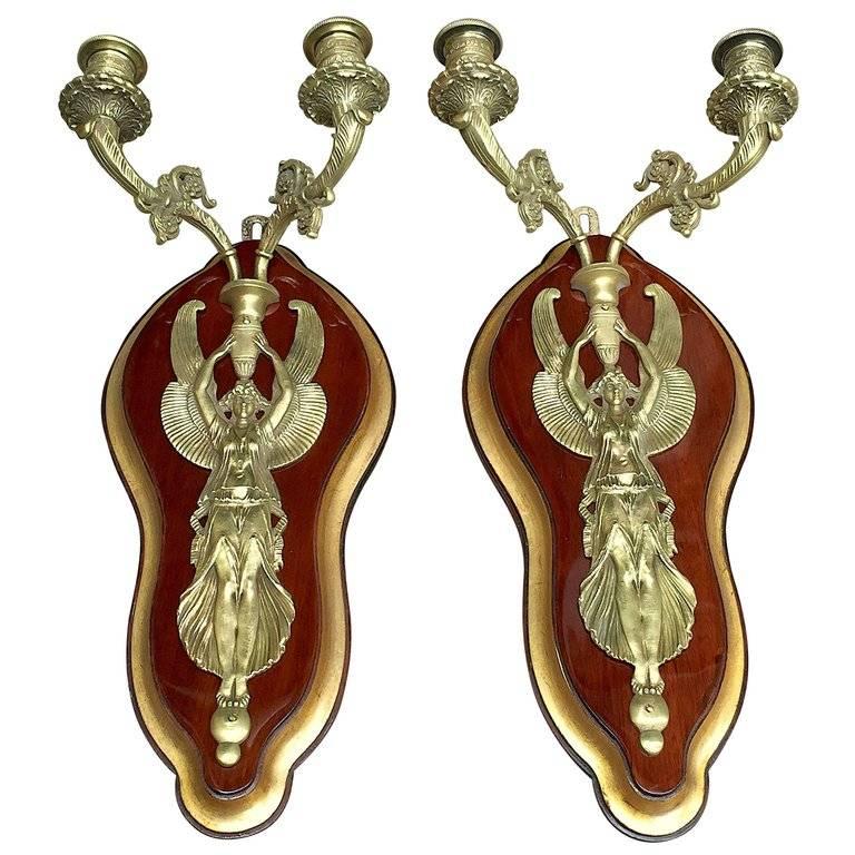 A pair of elegant French bronze two-armed figural wall lights with winged Victories, mounted on shaped cherrywood panels with bevelled gilt edges.
In perfect conditions, both wall candleholders have new European standard wiring and date back to