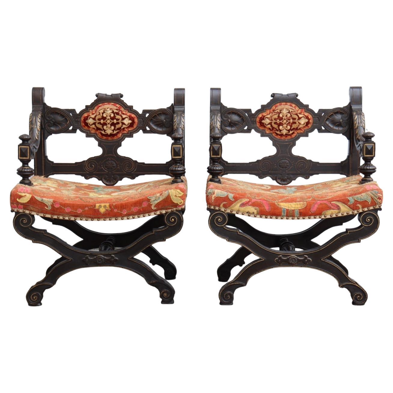 Pair of French Napoléon III Curule Armchairs
Moulded, carved, blackened wood, enhanced with gold. 
Open-banded back decorated with interlacing, X-base joined by an entretoise.
Older Polychrome trim embroidered with floral interlacing.
Circa