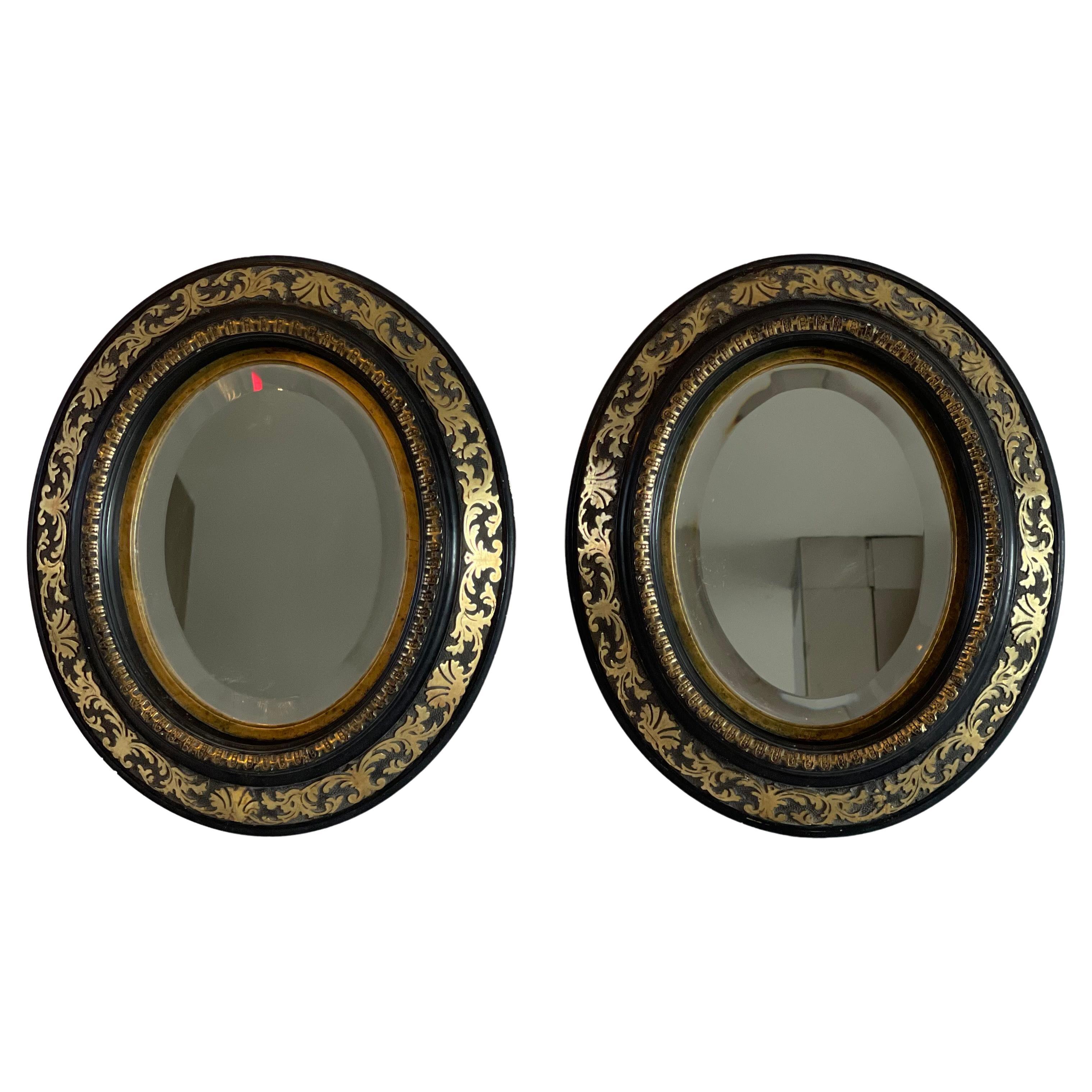 Coppia di specchi ovali del periodo Napoleone III in legno dipinto di nero e intarsiato con decorazioni in bronzo dorato, lo specchio è smussato.