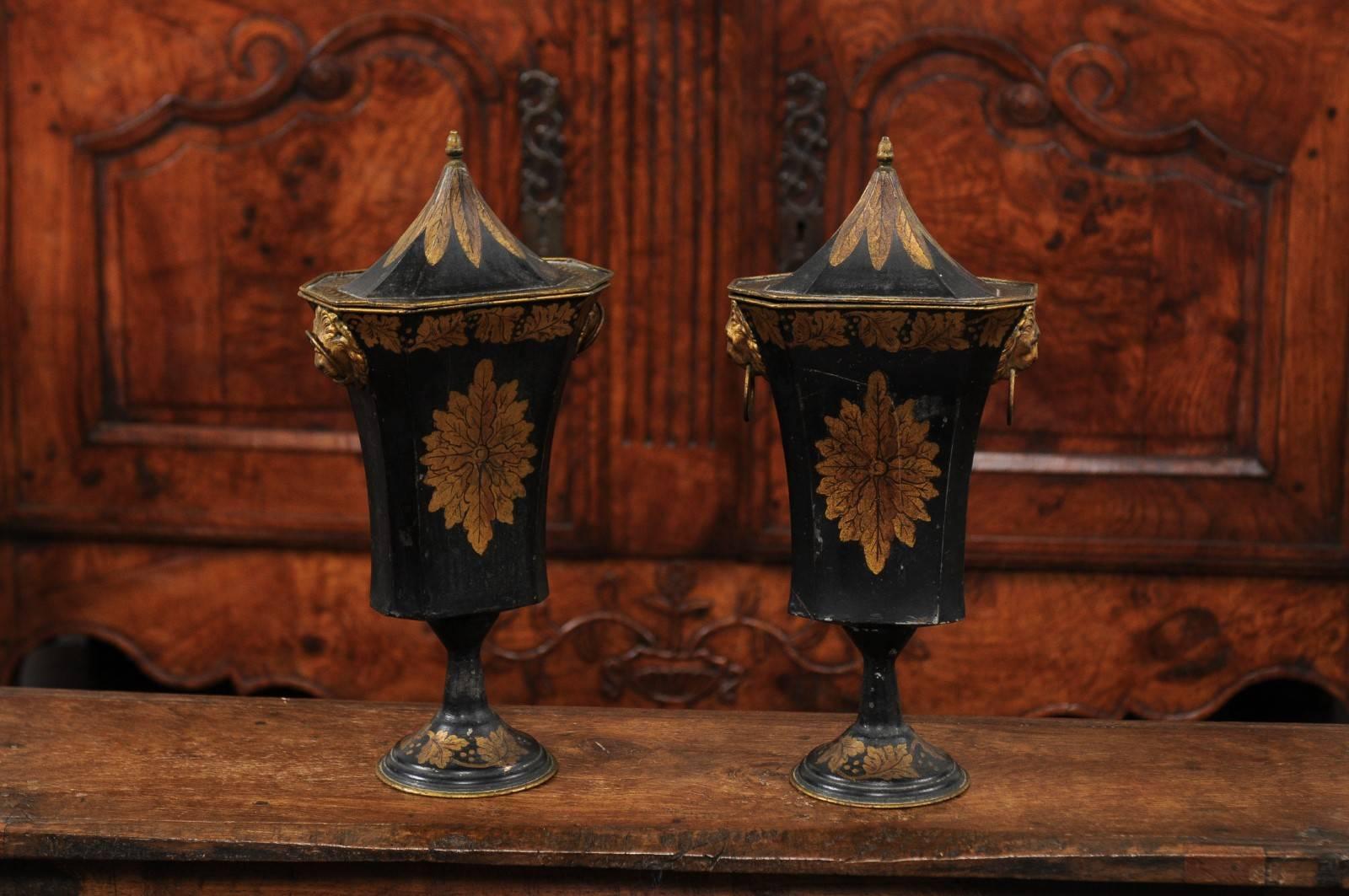 A pair of French Napoleon III period painted and gilded tôle urns with lids from the mid-19th century. Each of this pair of French urns features a pyramidal lid, adorned with gilded foliage that seems to be extending from the upper finial. The body,