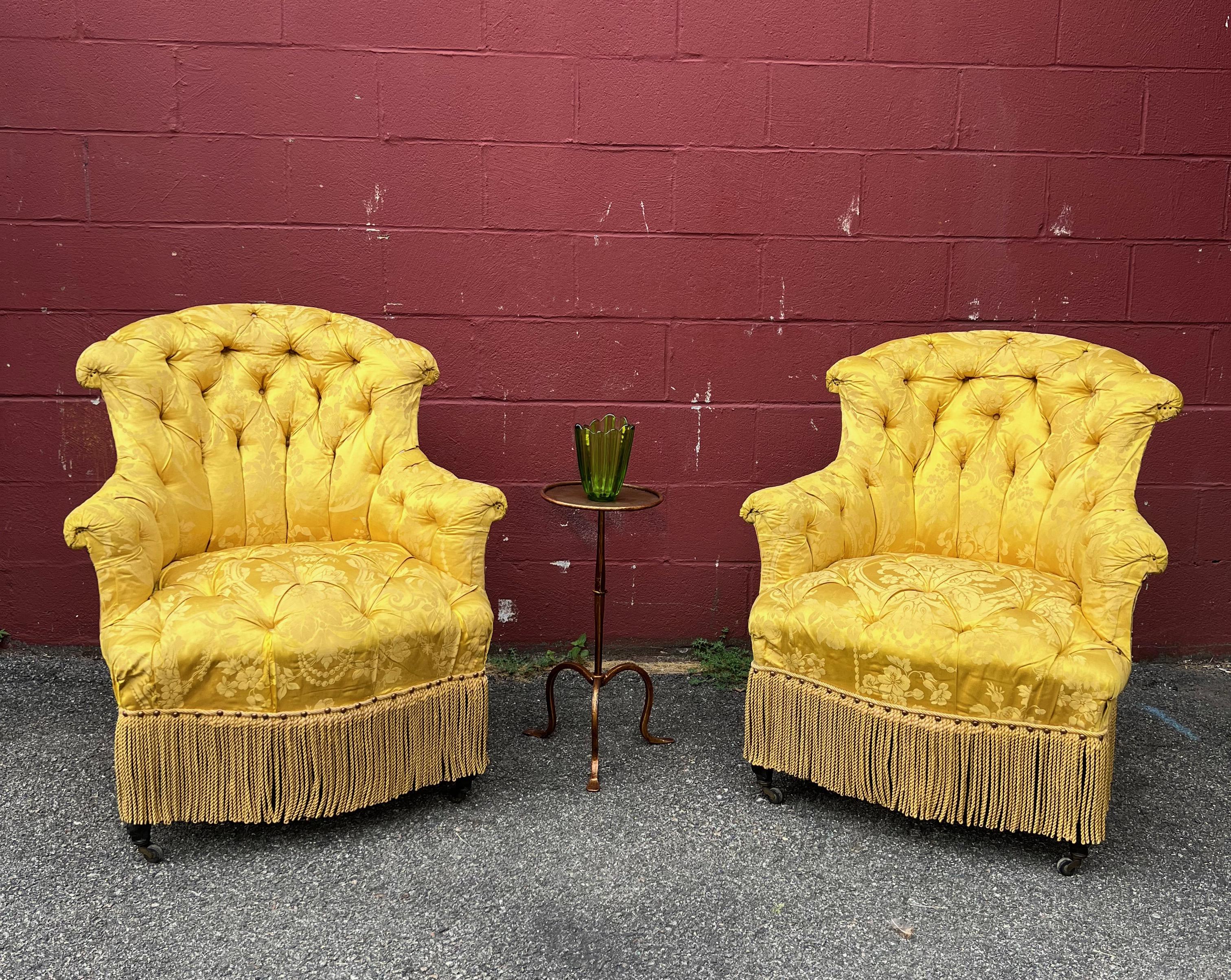 An  exquisitely tufted pair of French Napoleon III arm chairs with graceful rolled arms and backs. Both the back and seat are tufted in a yellow/ gold damask silk and the back is upholstered in a contrasting solid fabric. The chairs are finished off
