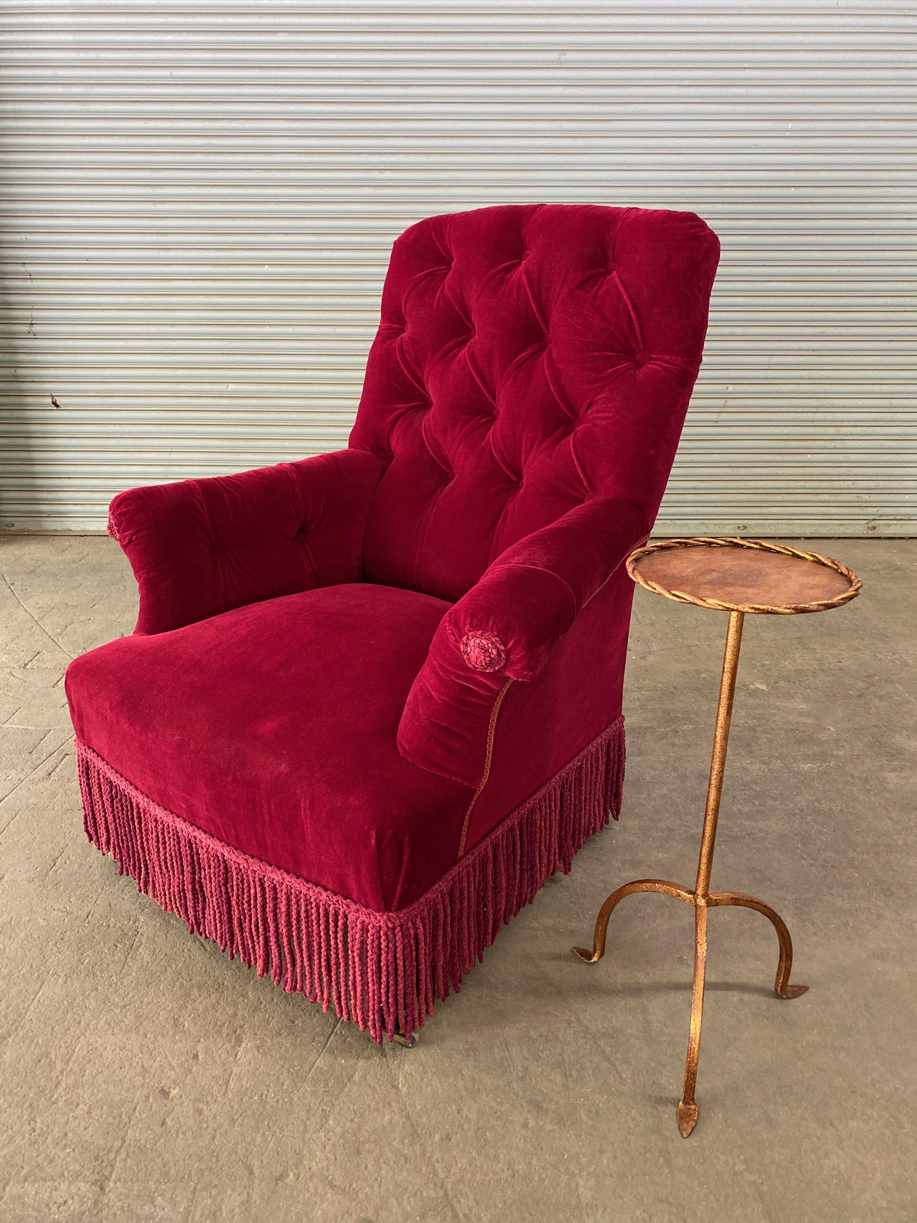 A pair of large French 19th century tufted armchairs upholstered in red velvet with matching bullion fringe. The armchairs are in very good vintage condition, and while the upholstery is not new, the fabric is clean and can be used. Sold as