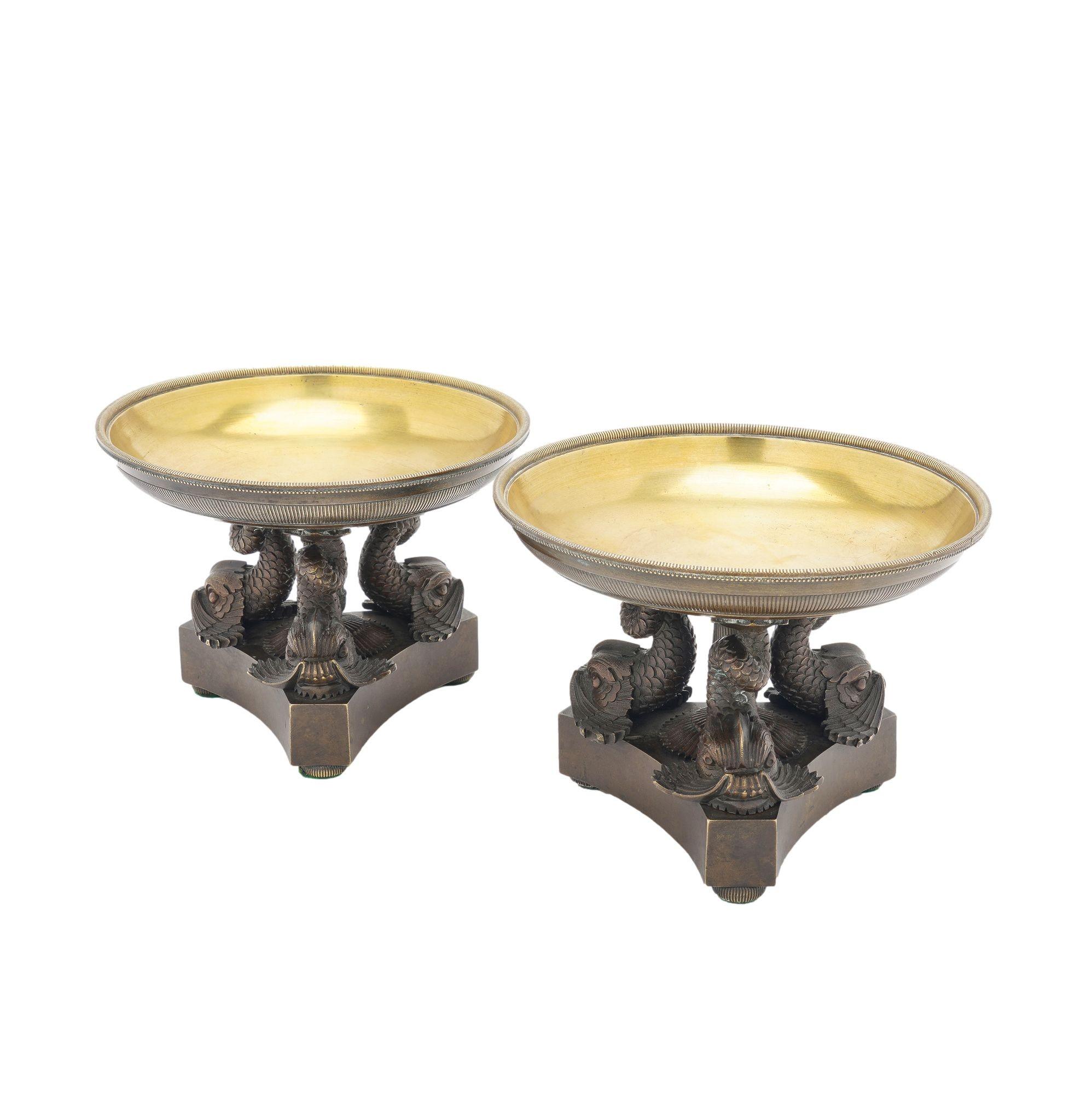 Coppia di tazze francesi neoclassiche in bronzo fuso. Il piatto lucido e poco profondo ha un bordo zigrinato ed è sostenuto da tre delfini su un basamento a treppiede con piedi a sfera zigrinati e soppressi.

Francia, circa 1800-25.