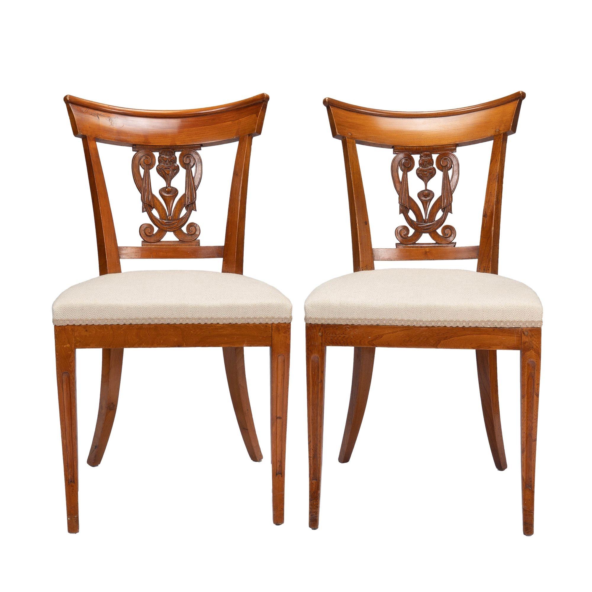 Pair of French neoclassic upholstered seat side chairs. The chairs are defined by sabre front and raked rear legs which support an upholstered boxed seat. The splayed upper leg posts are joined by a lower back rail and dramatically carved cut crest