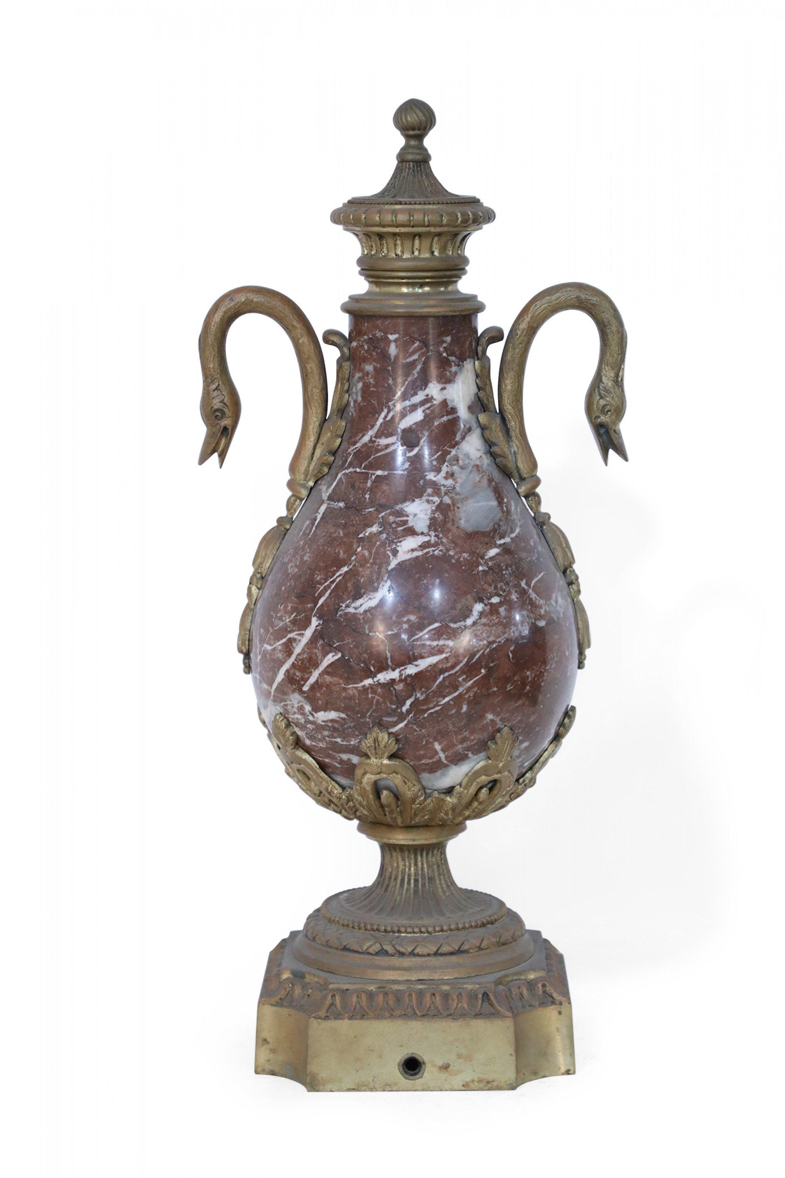 Pair of French Neoclassical decorative urns made from globular, burgundy marble bodies nestled within decorative bronze cradles held by square bases, accented in two swooping bronze duck handles and topped with ornate bronze finials (PRICED AS PAIR).