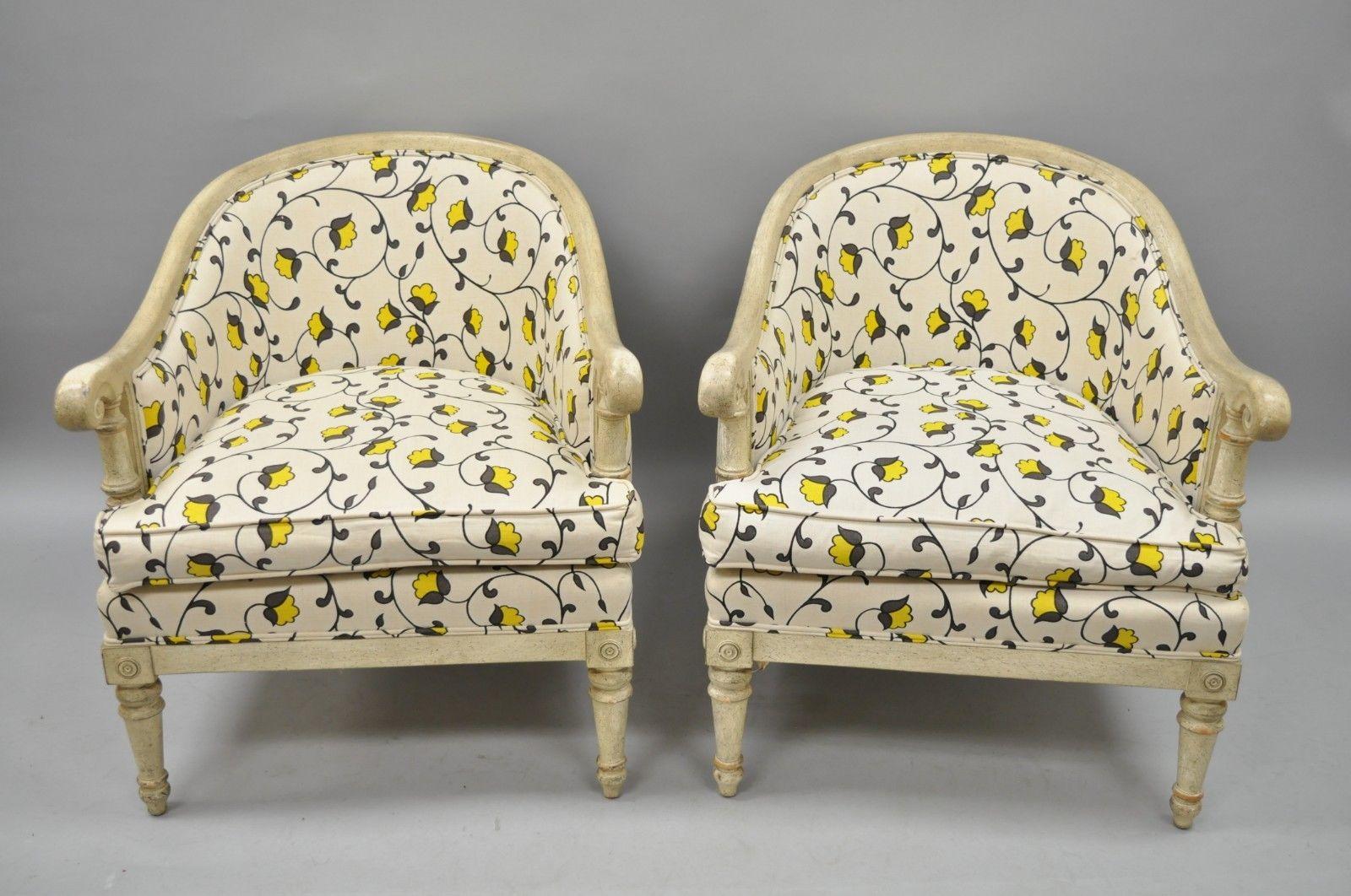 Pair of French neoclassical/Directoire style cream distress painted barrel back club chairs. Item features solid carved wood frames, shapely barrel backs, tapered legs, rolled arms, yellow floral print upholstery, cream distress painted finish, and