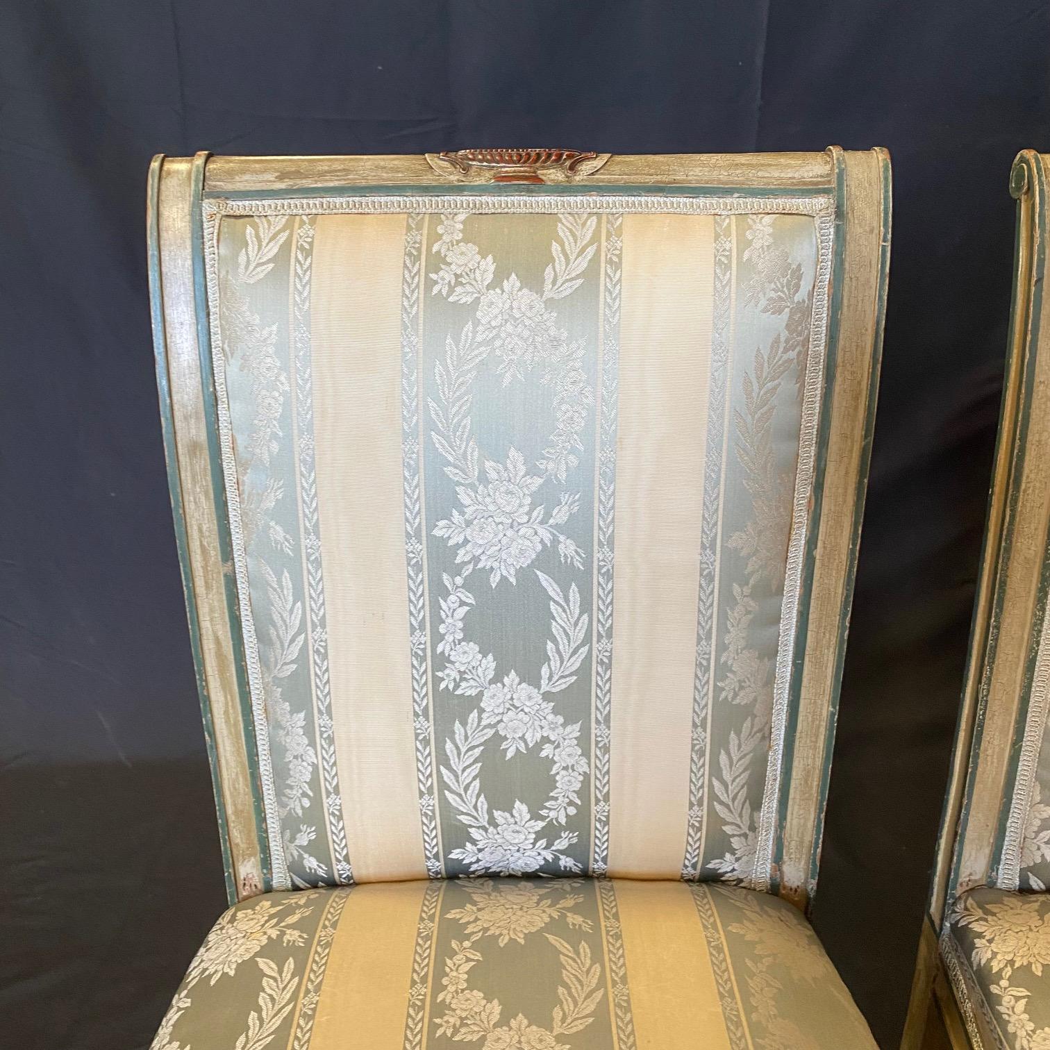 French neoclassical giltwood dining chairs featuring a compound shaped rectangular back, carved foliate crest, ornate painted frame with decorative embellishments, padded back and seat upholstered in a pale gold and green stripe patterned fabric,